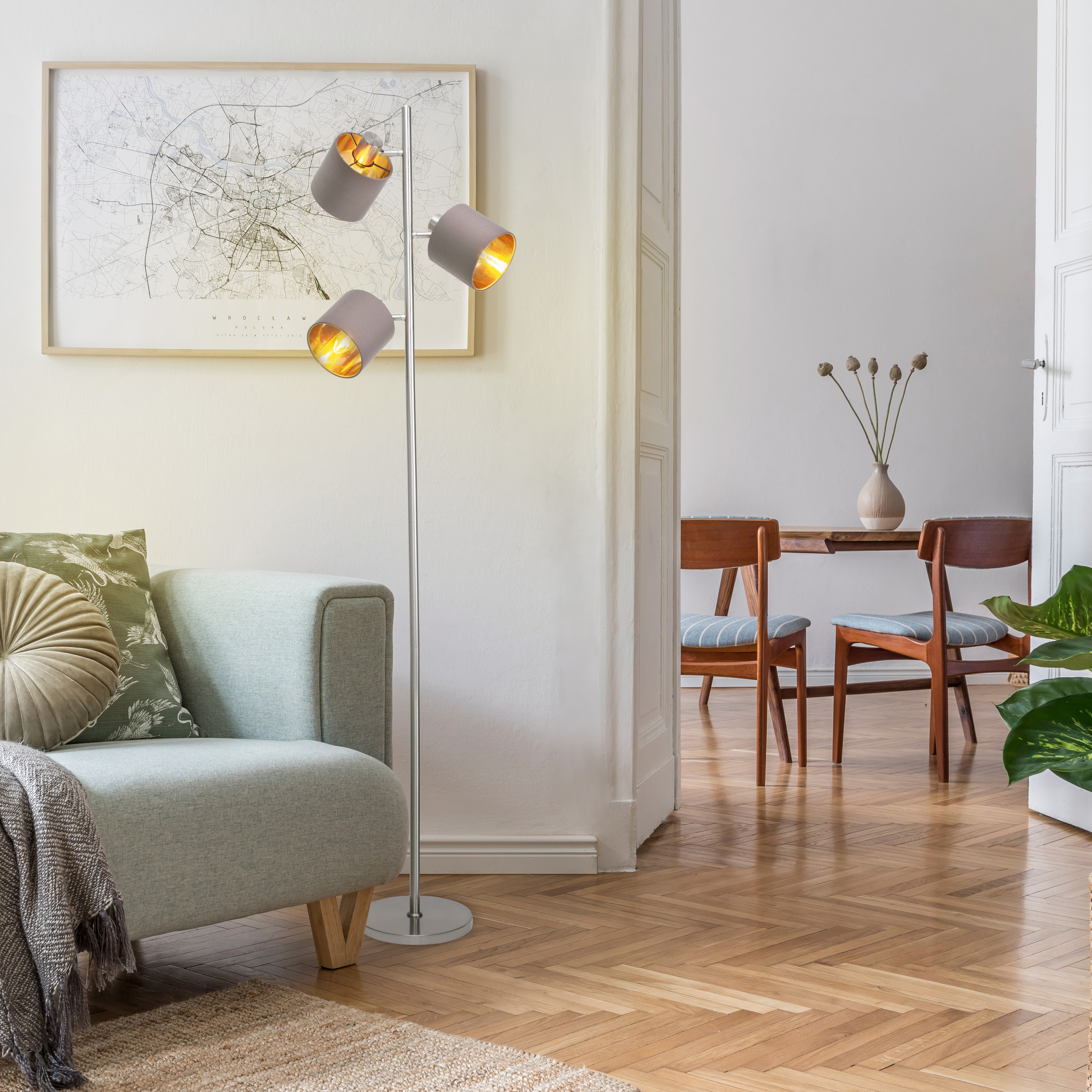 Ein Raum mit Stehlampe, Sofa und Karte an der Wand. Es gibt einen Essbereich mit Stühlen und einem Tisch.