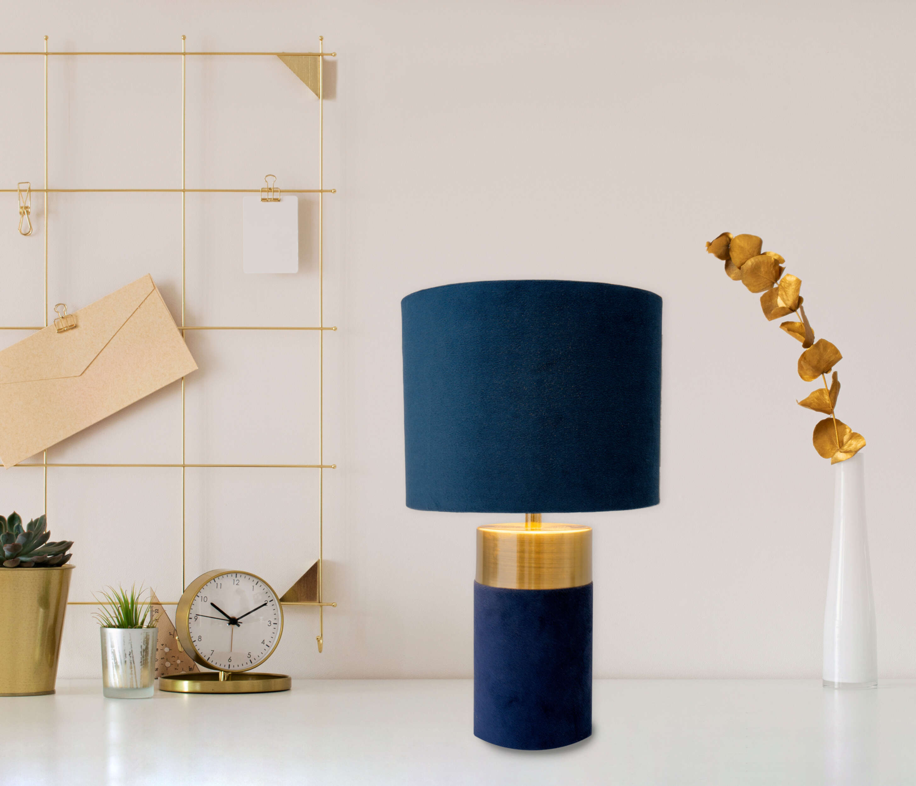Blaue Lampe mit goldenem Sockel auf einem weißen Schreibtisch. Goldenes Gitter und Vase im Hintergrund.