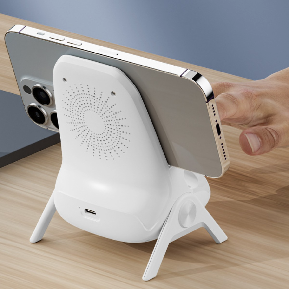 Weißes Telefonladegerät mit Telefon. Eine Hand berührt das Telefon. Holztisch im Hintergrund.