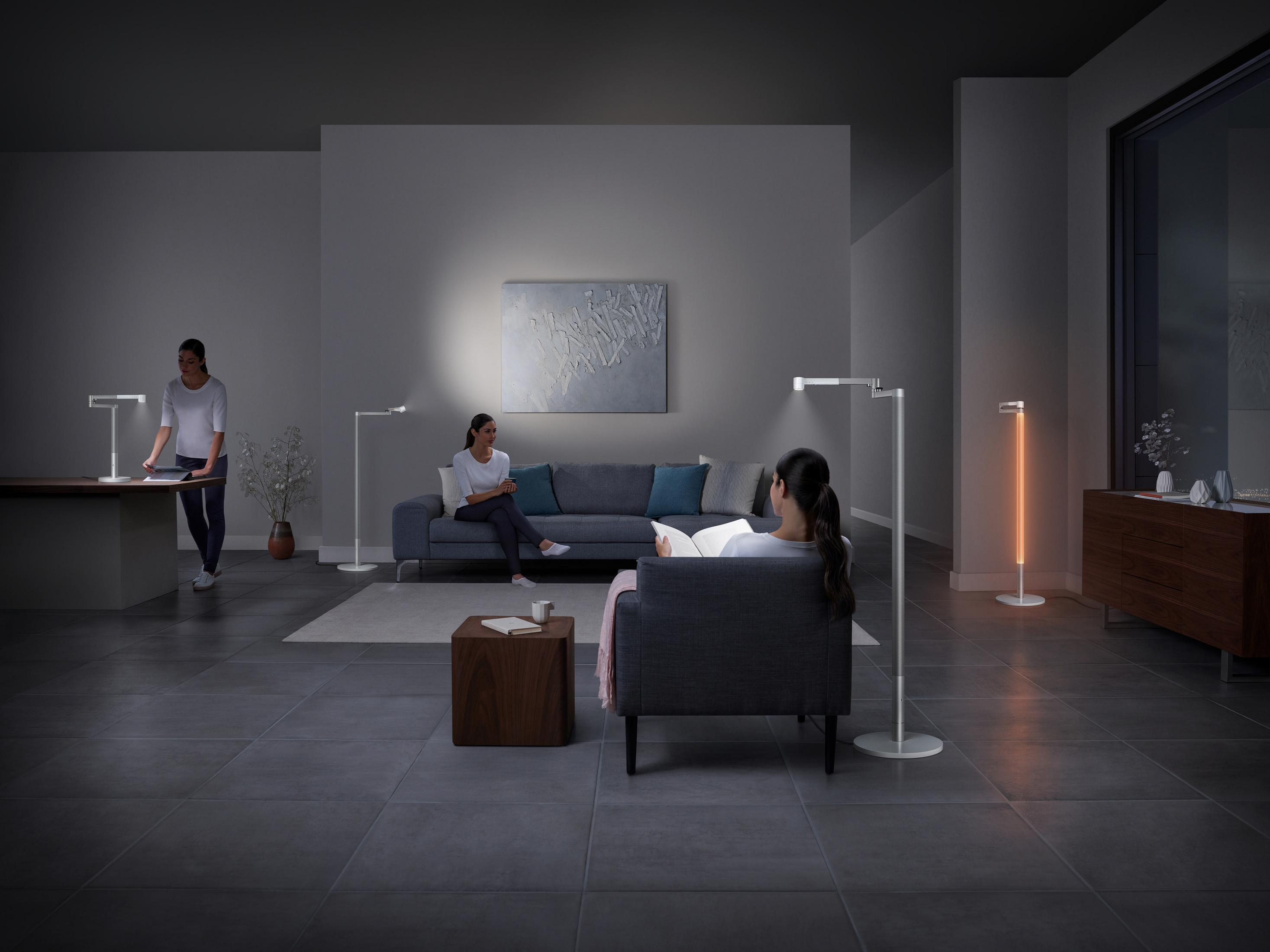 Wohnzimmer mit Personen, Lampen, Sofa und einem Gemälde; nachts beleuchtet.