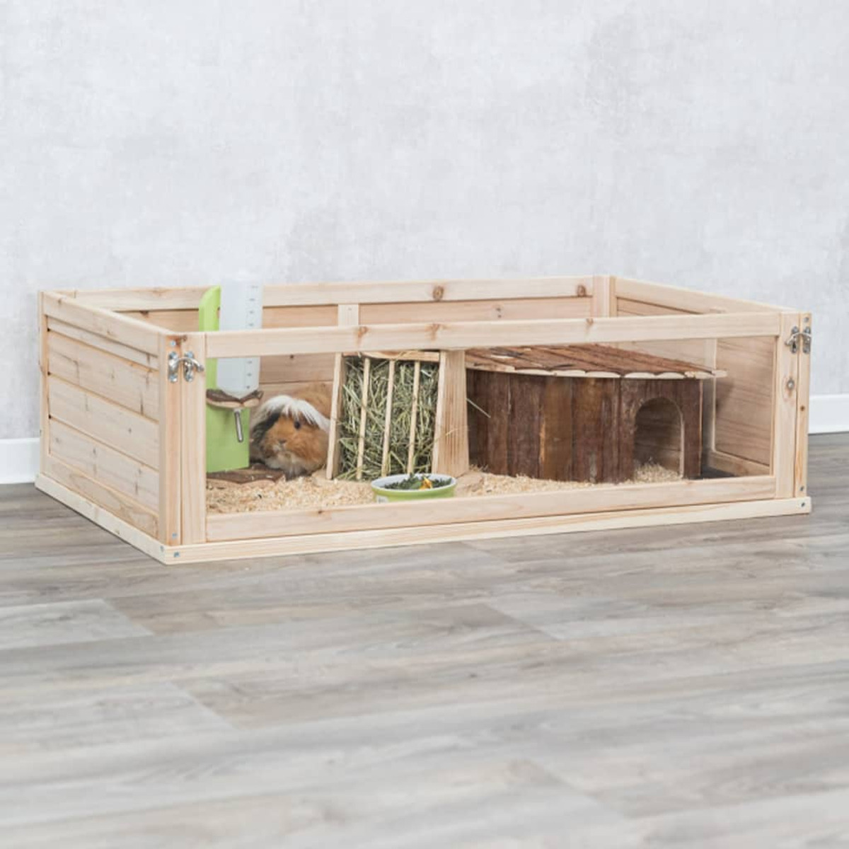Recinto de madera para mascotas con un conejillo de indias dentro. Tiene una casa de madera, comida y agua.