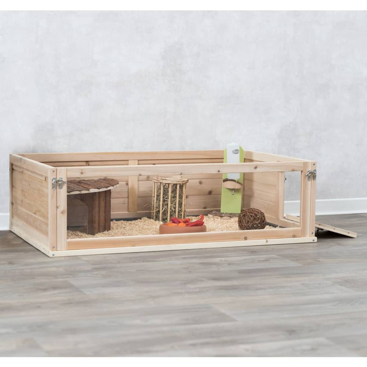 Recinto para mascotas de madera con casa, comida y accesorios, sobre suelo de madera.