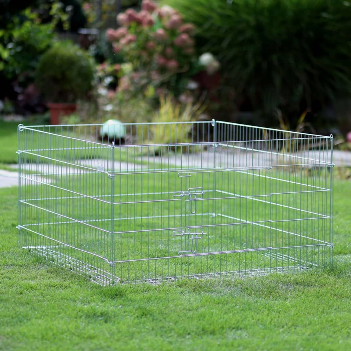 Ein quadratischer Metall-Haustierkäfig auf grünem Gras, mit weißem Hintergrund.