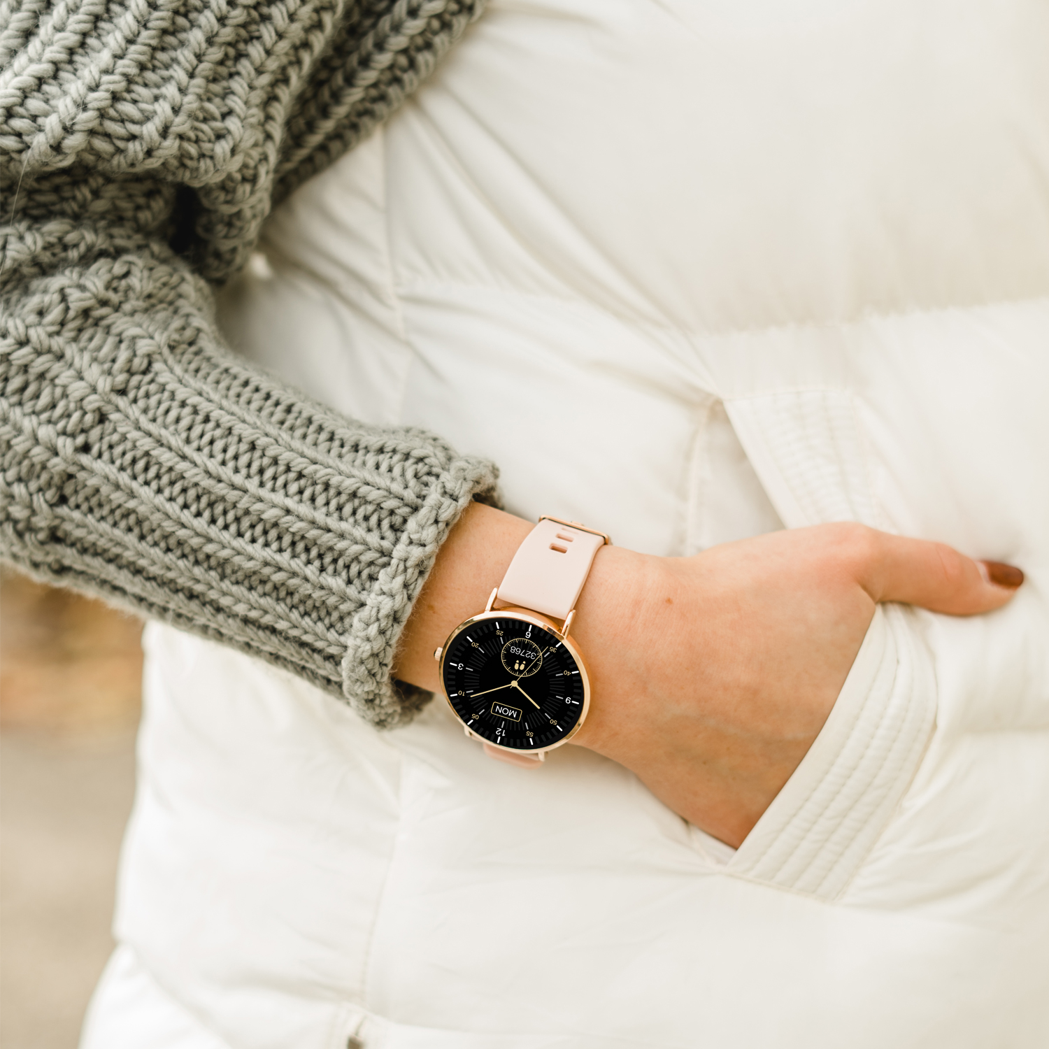 Das Handgelenk einer Frau mit einer roségoldenen Uhr und einem cremefarbenen Armband.