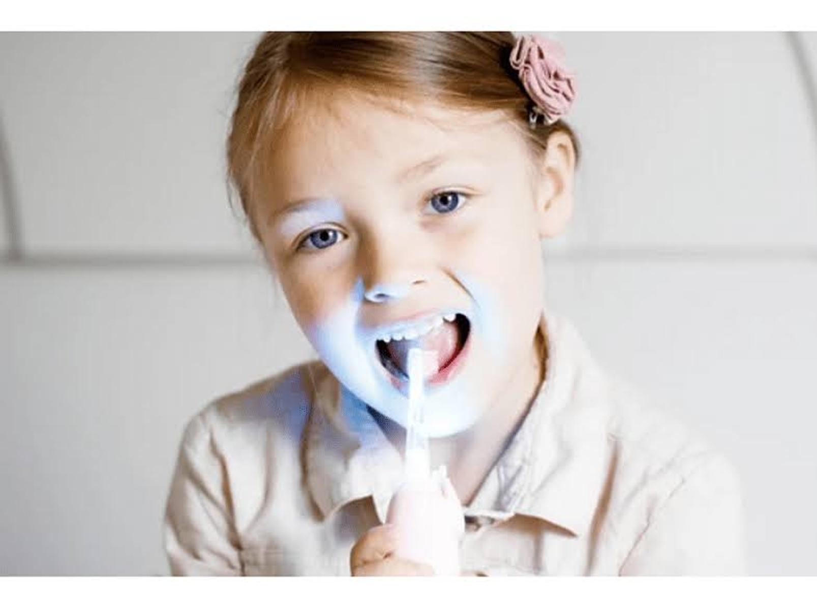 Ragazza con luce blu sui denti, usa un dispositivo per sbiancare i denti.