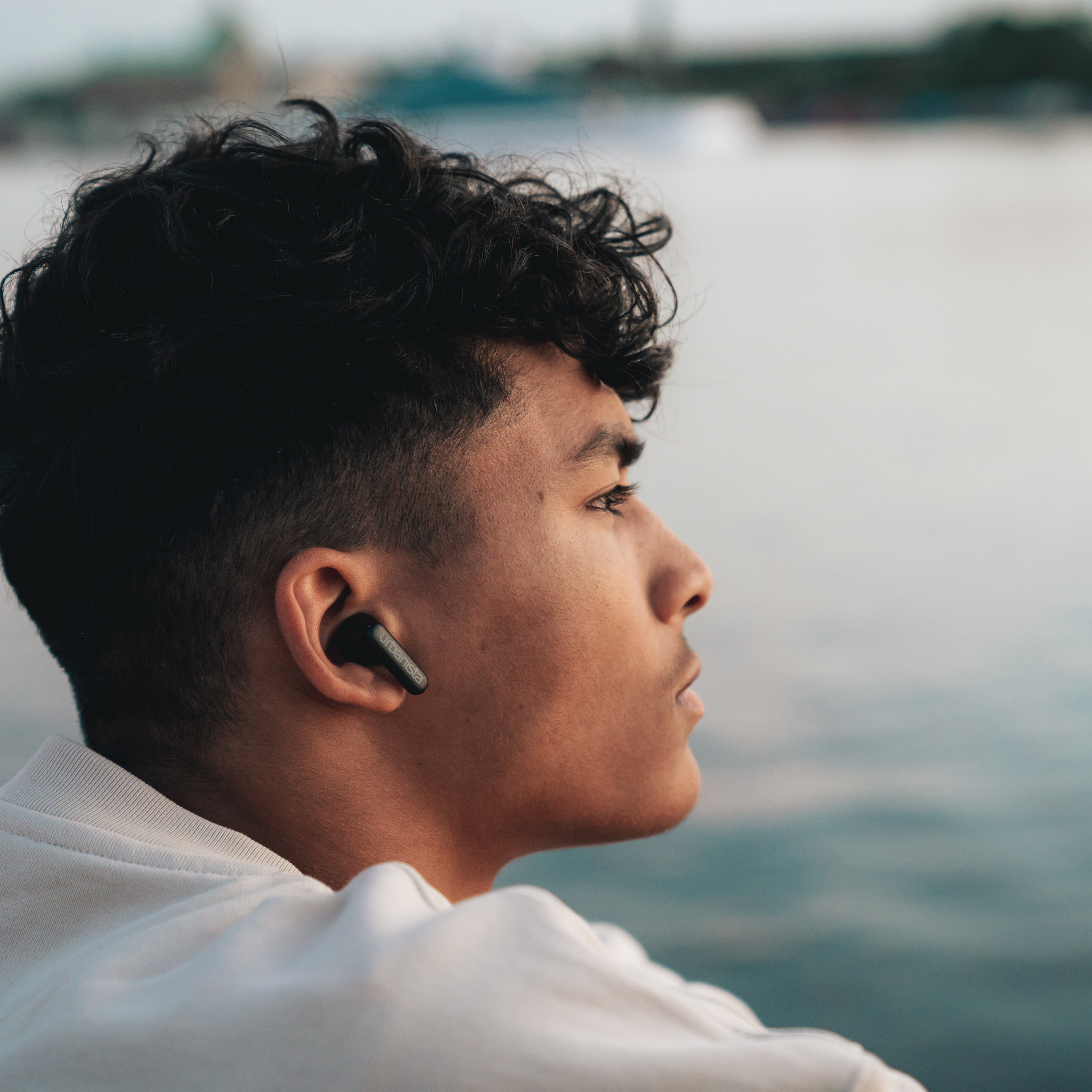 Młody mężczyzna w czarnych słuchawkach patrzy w bok w pobliżu wody.