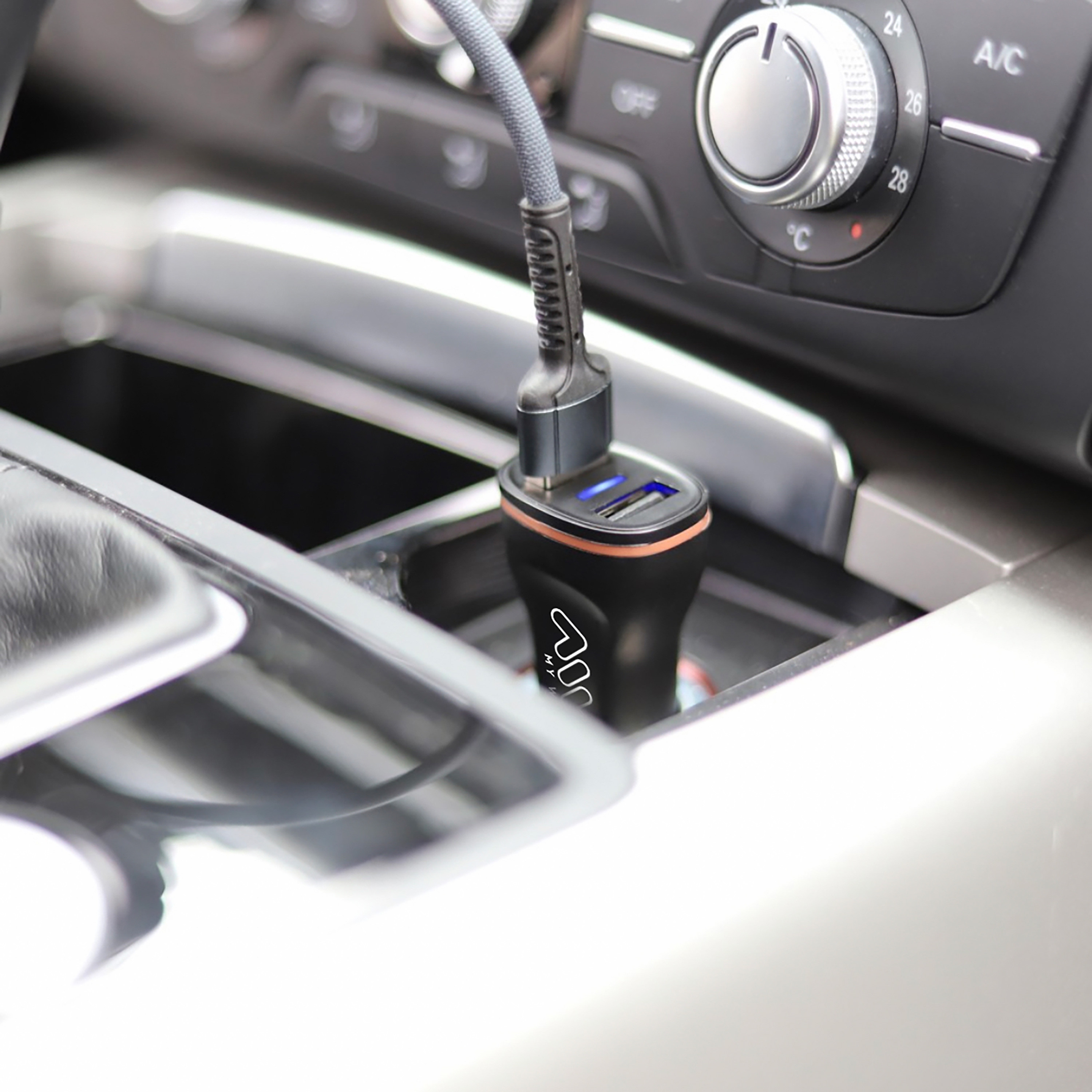 Un cargador de coche enchufado en la consola de un coche. Tiene dos puertos USB y un anillo naranja.