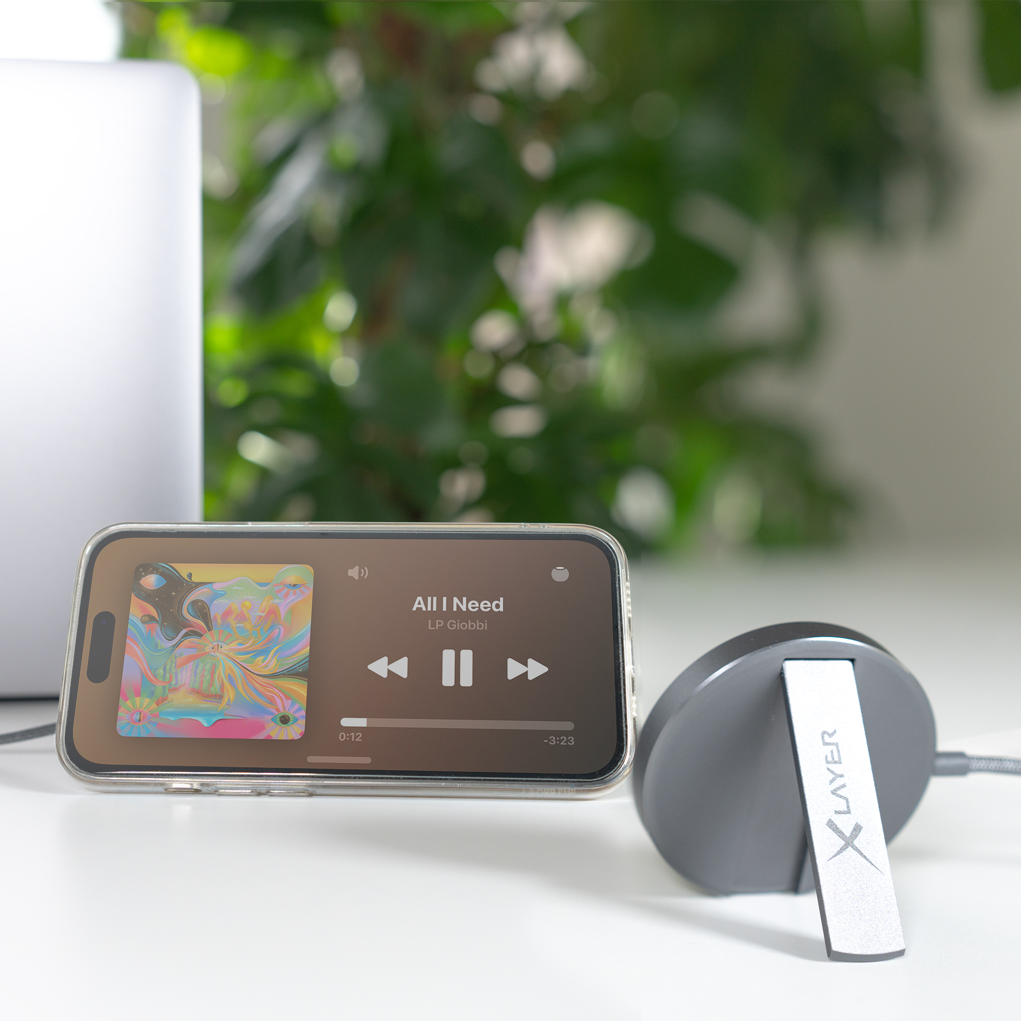 Ein Telefon zeigt Musiksteuerung, liegt auf weißer Oberfläche, mit grauem Lautsprecher.