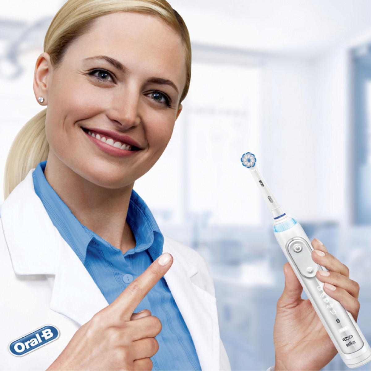 Donna bionda in camice bianco, tiene uno spazzolino elettrico, indicandolo con un sorriso.