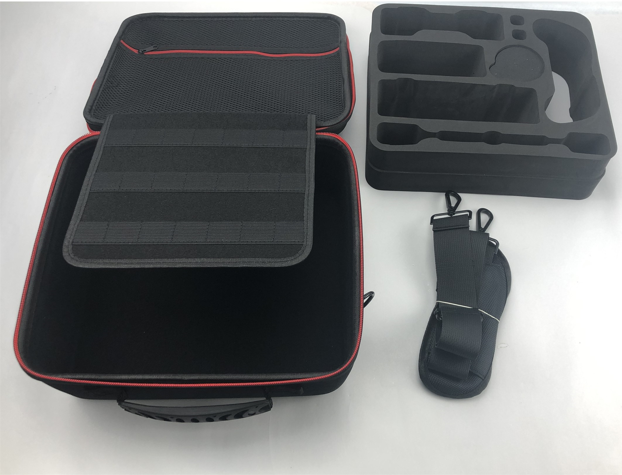 An open black suitcase containing a black foam insert, a lid with pockets, and a shoulder strap.