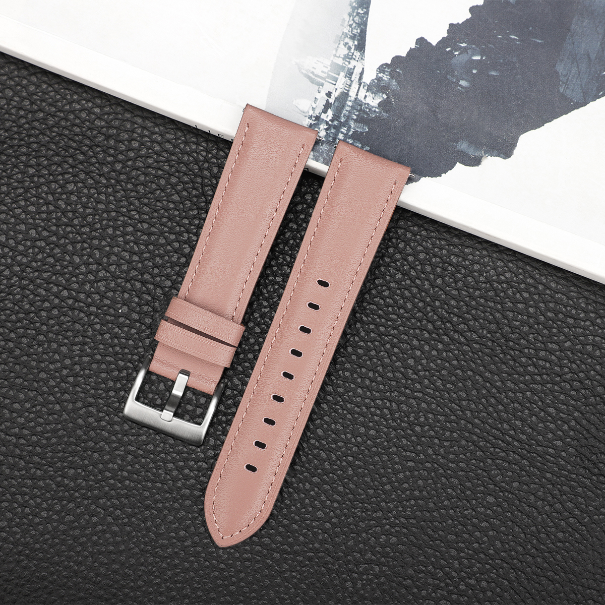 Zwei rosa Lederarmbänder mit einer silbernen Schnalle, die auf einer dunklen strukturierten Oberfläche liegen.