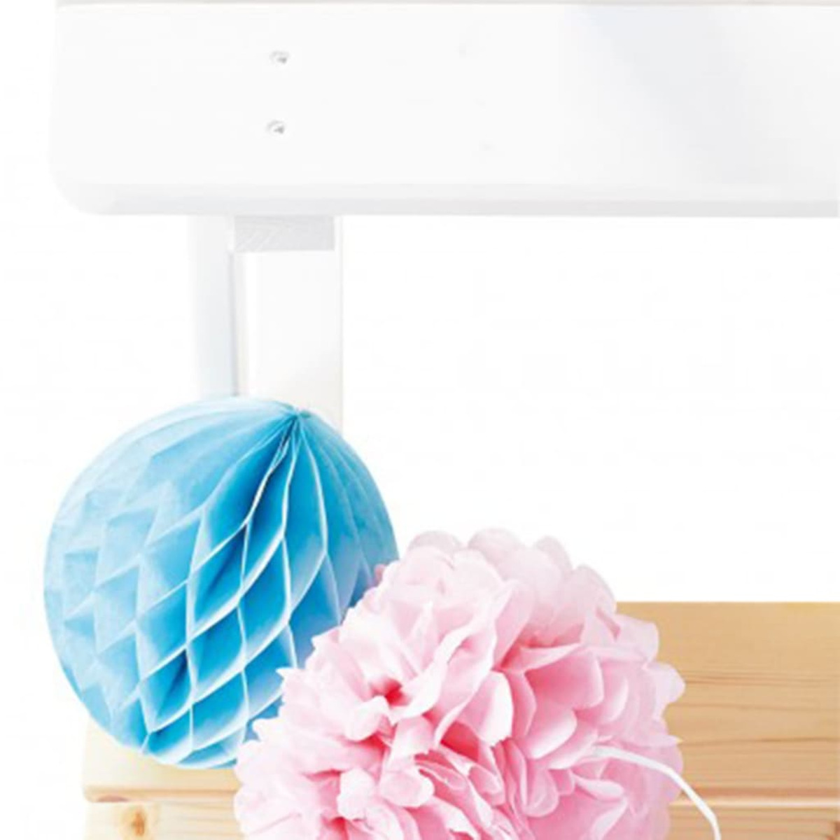 Zwei bunte Papierdekorationen, eine blau, eine rosa, mit weißem Hintergrund, Holzoberfläche.