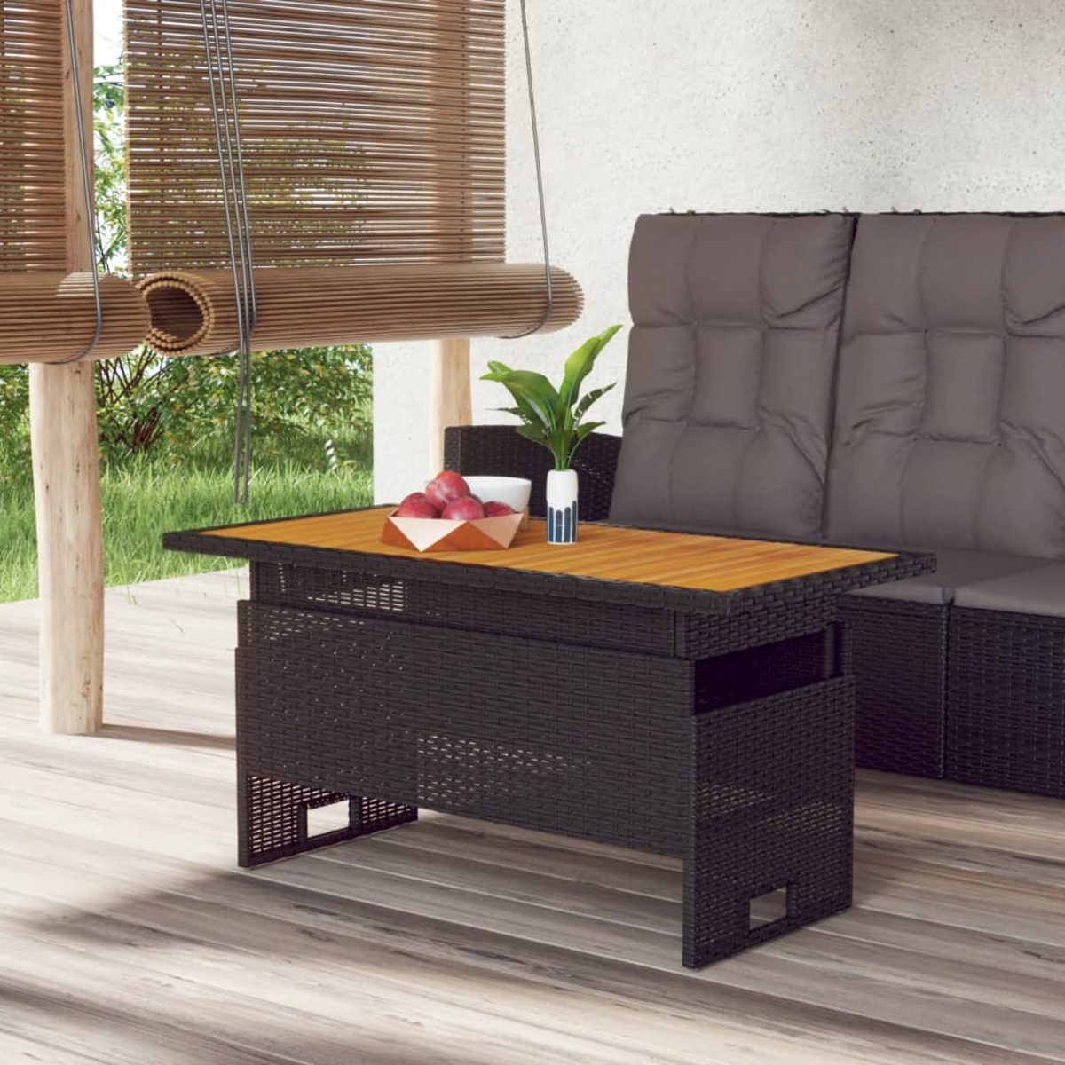 Ein schwarzer Rattantisch mit Holzplatte, eine Pflanze und ein Sofa im Hintergrund.