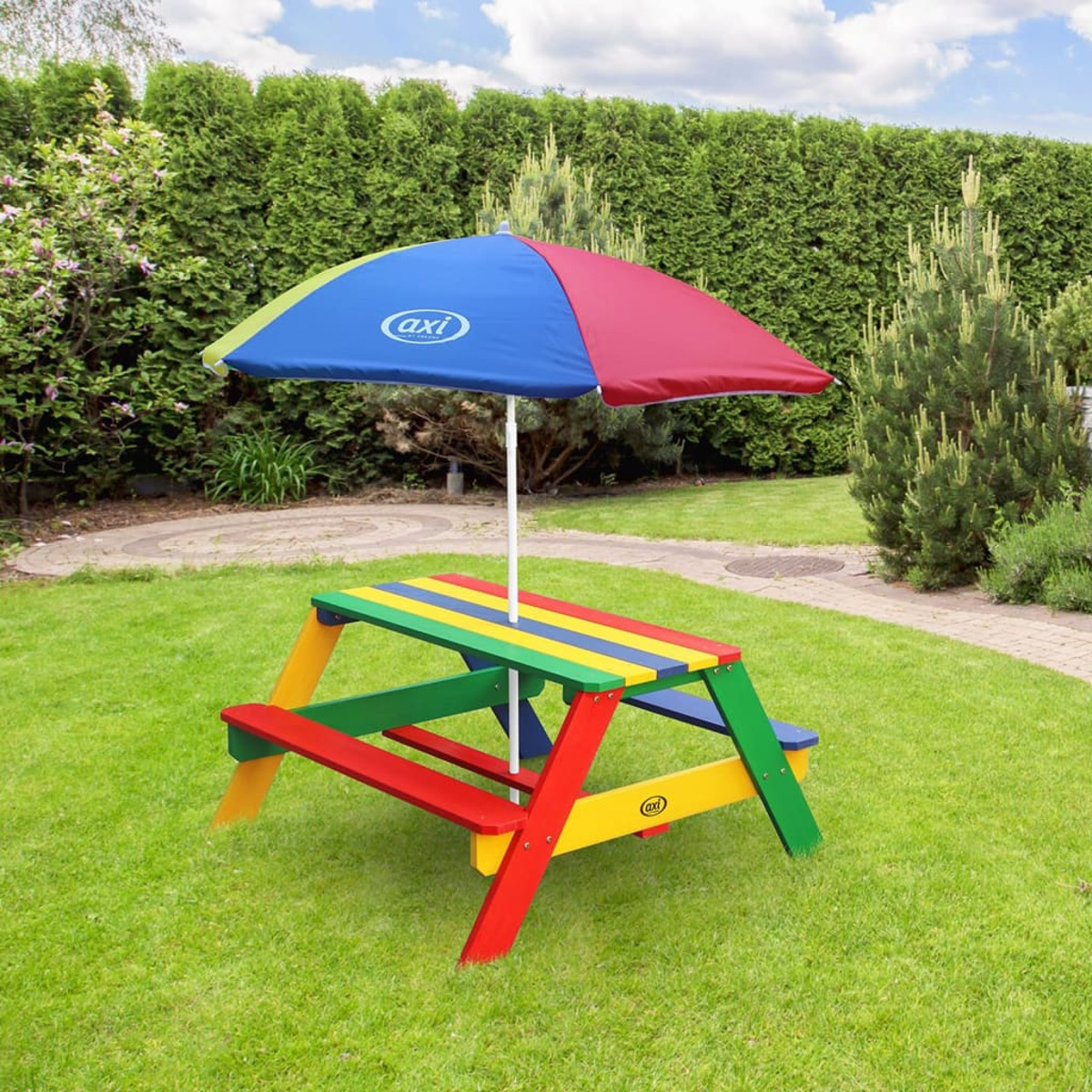 Bunter Picknicktisch mit Sonnenschirm im Rasen. Grüne Hecke im Hintergrund.