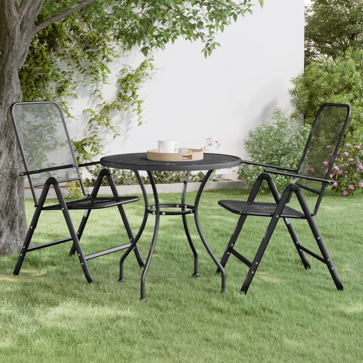Zwei schwarze Metall-Klappstühle und ein Tisch auf Gras, mit Baum und Grün im Hintergrund.