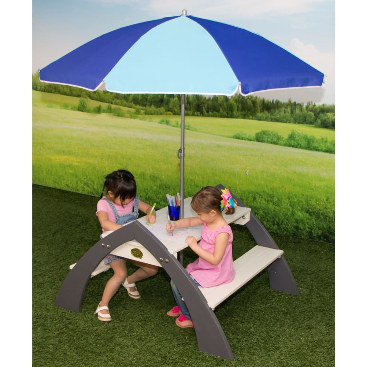 Kinder zeichnen an einem Picknicktisch unter einem blauen Schirm.