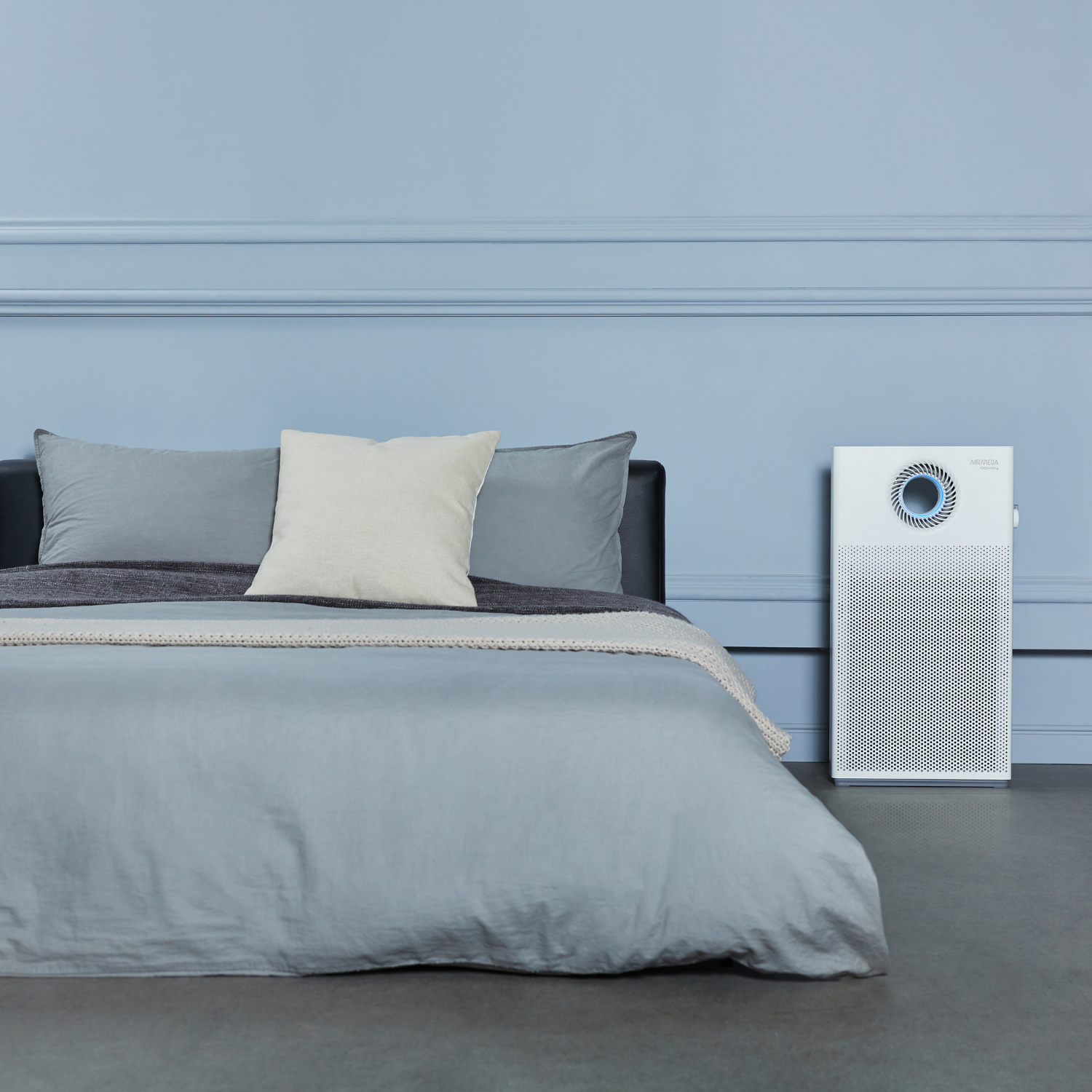 Schlafzimmer mit Bett, blauen Wänden, Luftreiniger, grauer Bettwäsche, weißem Kissen.