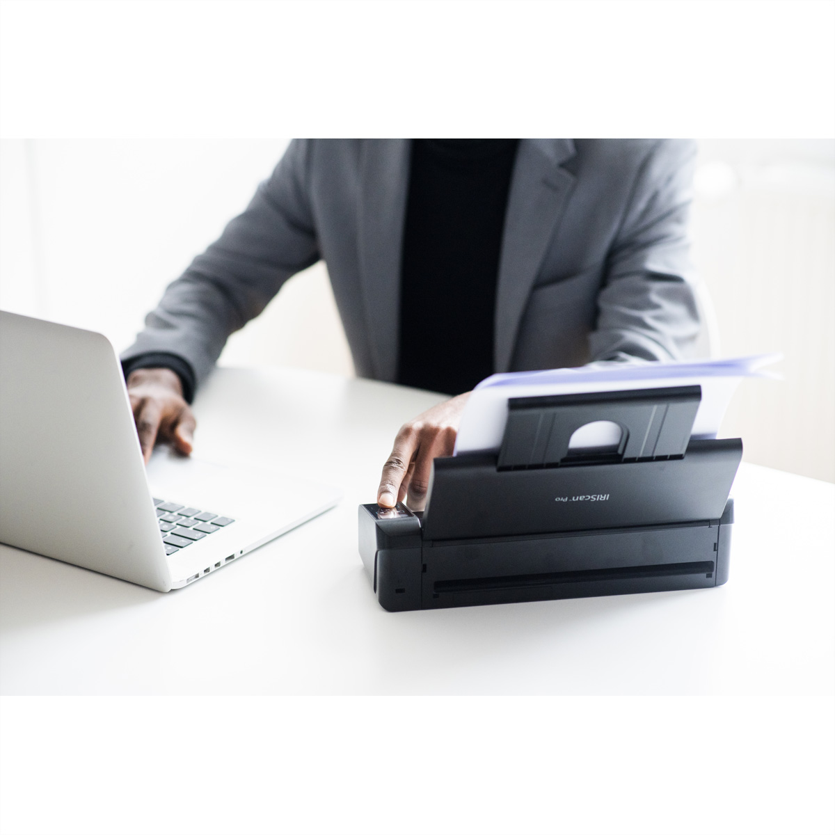 Person verwendet Drucker. Der Drucker ist schwarz, Papier ist eingelegt, Laptop offen.