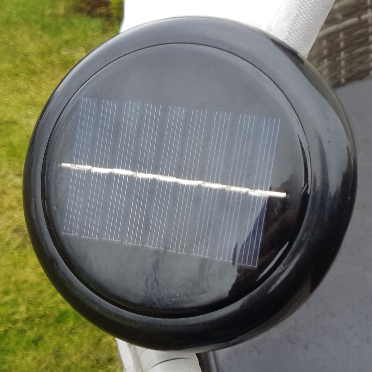 Schwarzes kreisförmiges Solarpanel mit Gittermuster auf grauer Oberfläche.