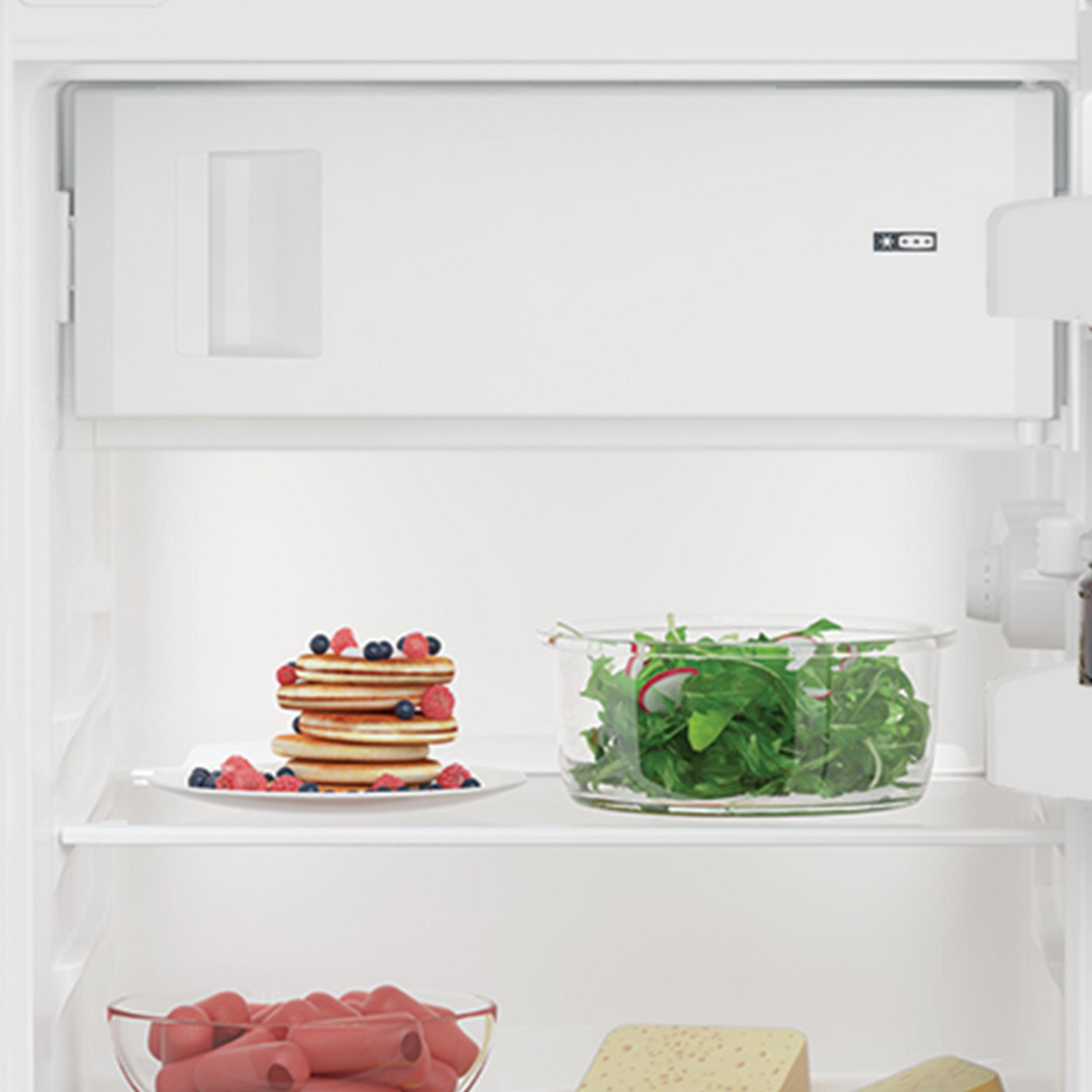 Offener Kühlschrank mit Pfannkuchen, Salat und anderen Lebensmitteln.