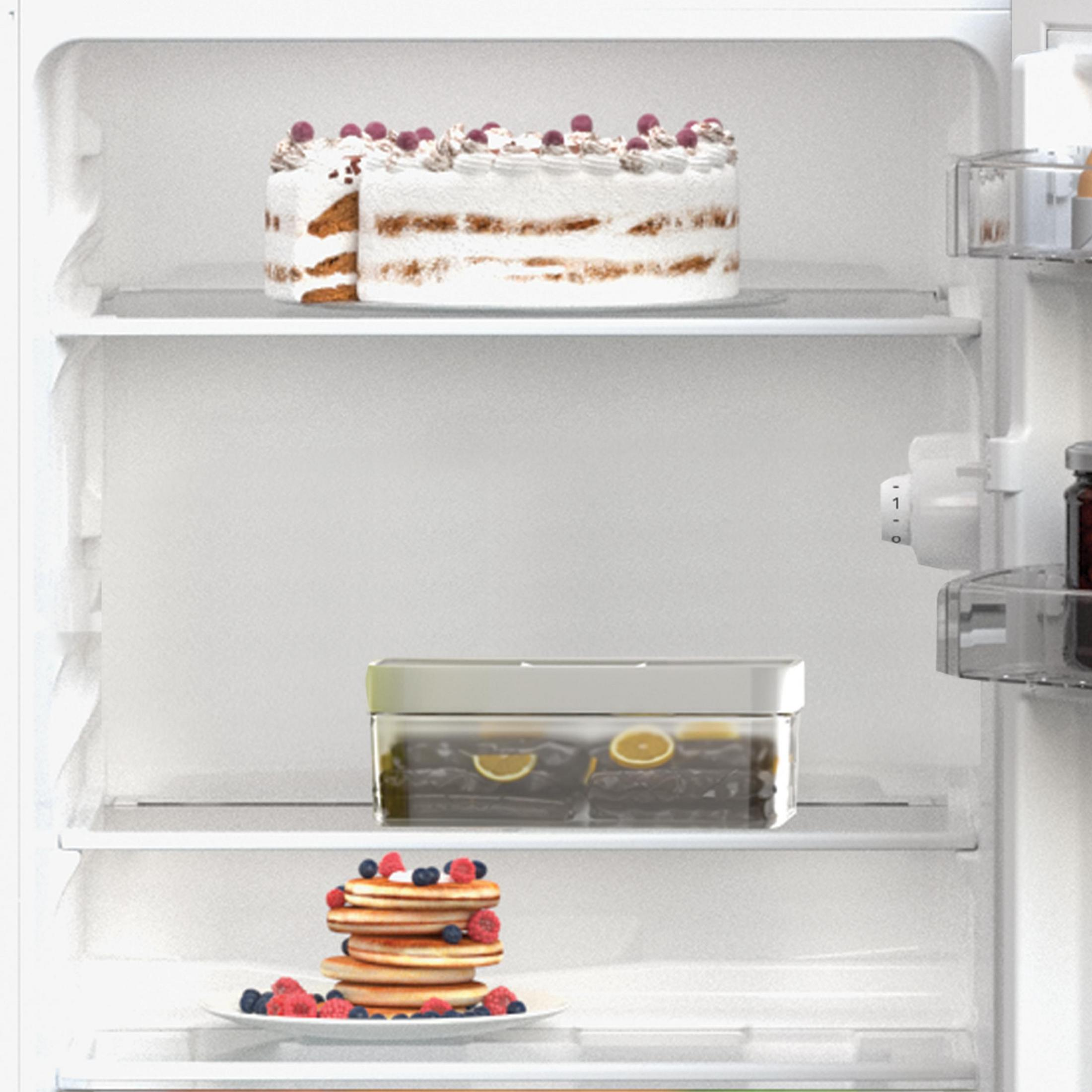 Interno di un frigorifero con torta, pancake e un contenitore di cibo sugli scaffali.