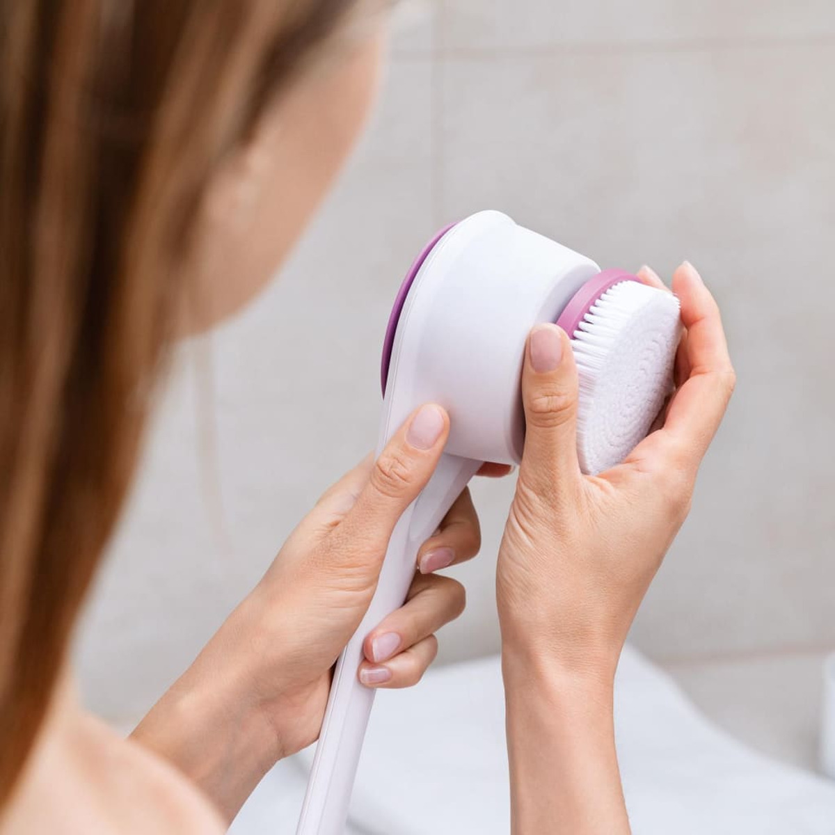 Personne tenant une brosse de douche blanche et violette. Focus sur la tête de brosse.