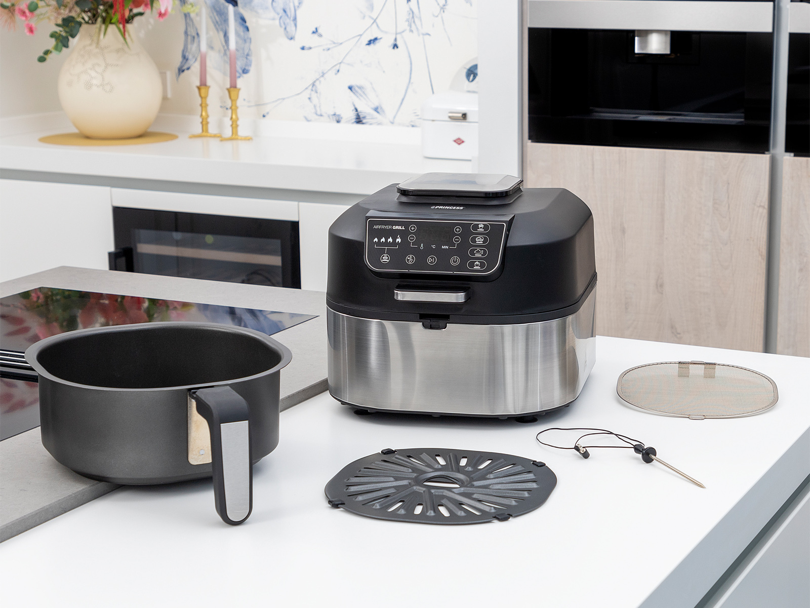 Frytkownica powietrzna z akcesoriami na białej powierzchni z tłem kuchni.