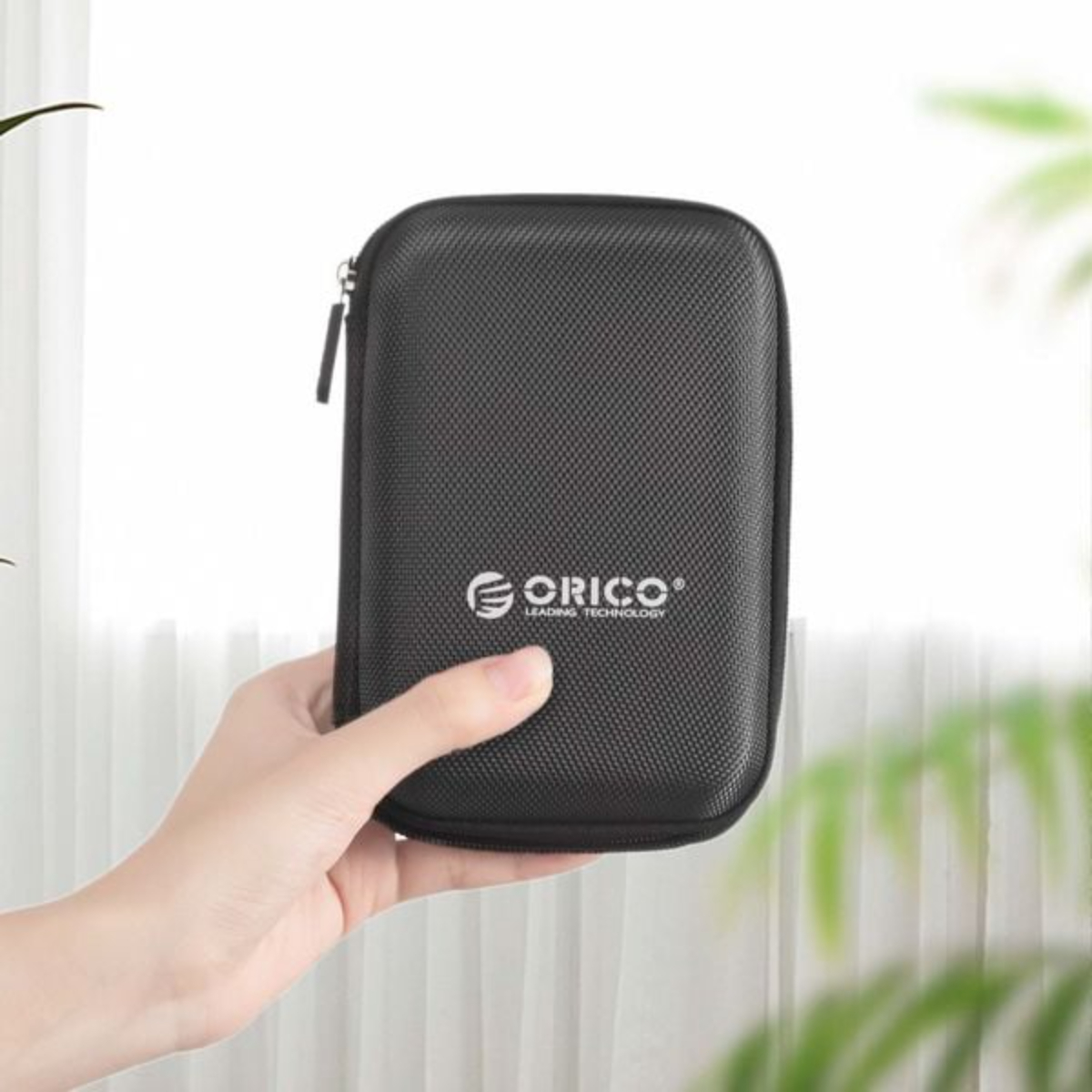 Eine Hand, die eine schwarze, mit Reißverschluss versehene Hülle mit dem Logo 'ORICO' hält, vor einem Hintergrund.