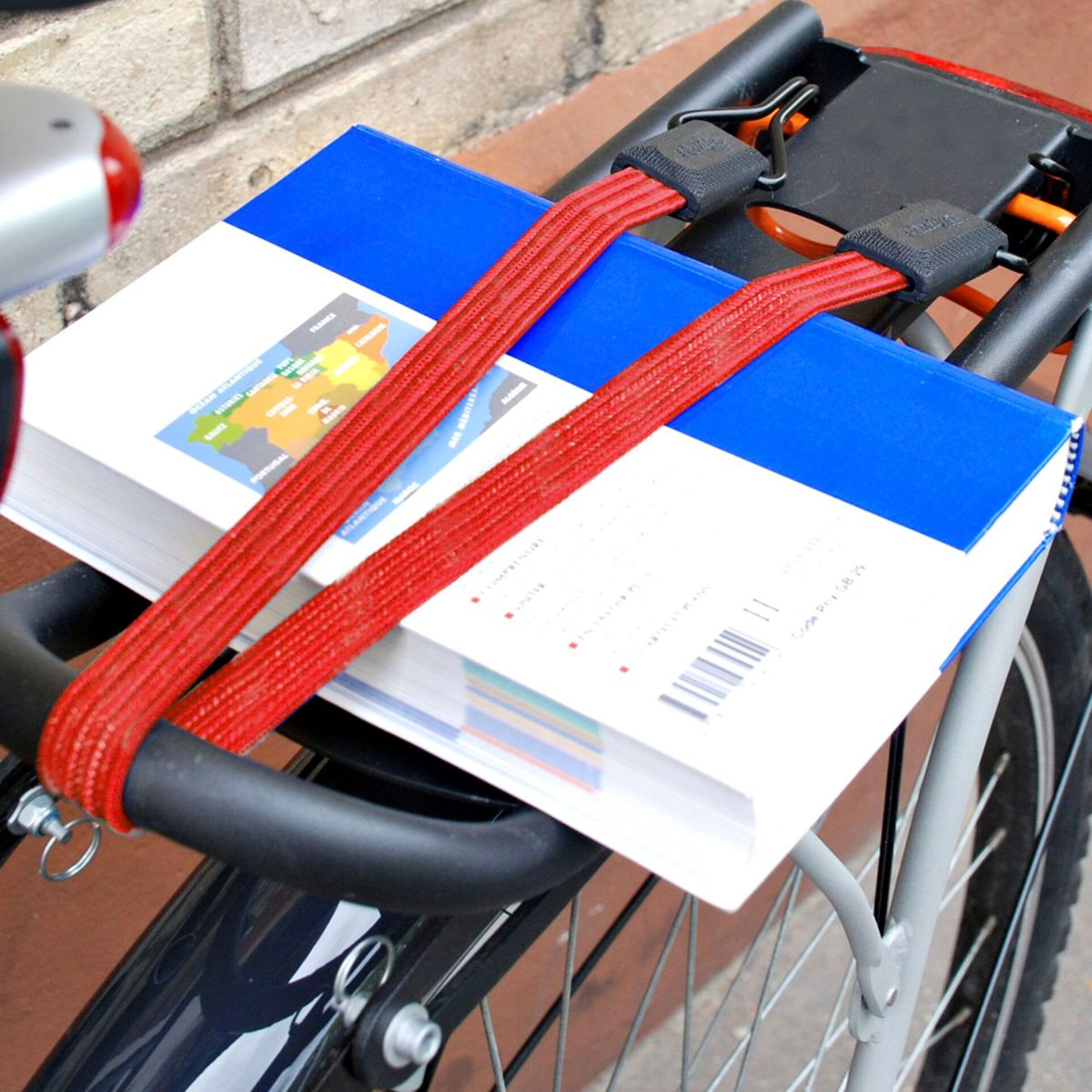 Un libro blu e bianco fissato con due cinghie rosse sul portapacchi di una bicicletta.
