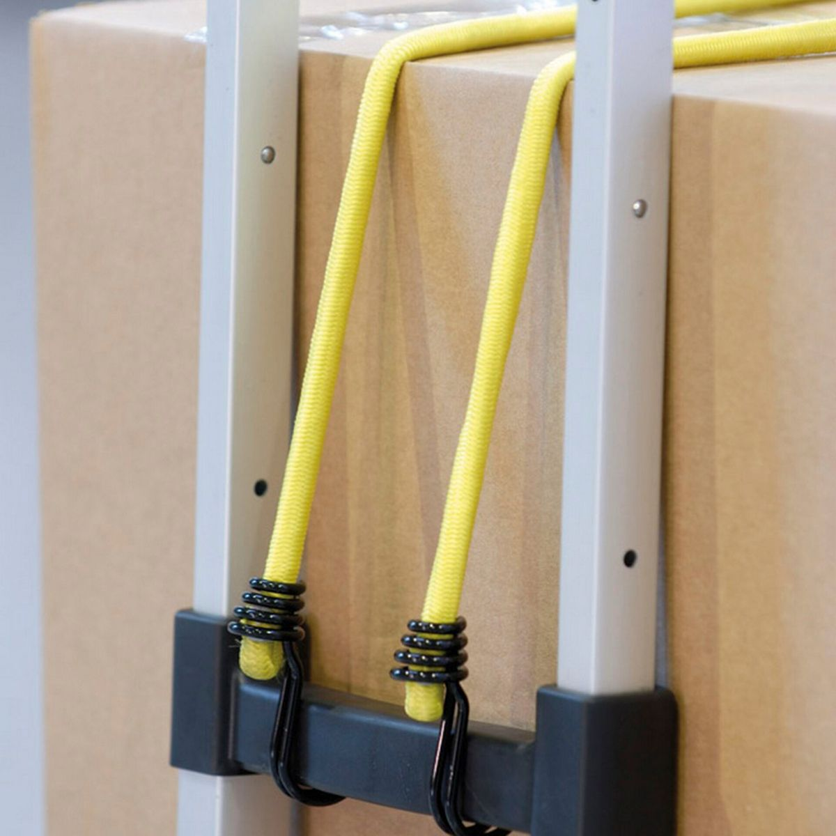 Un cavo elastico giallo assicura una scatola di cartone su un carrello metallico.