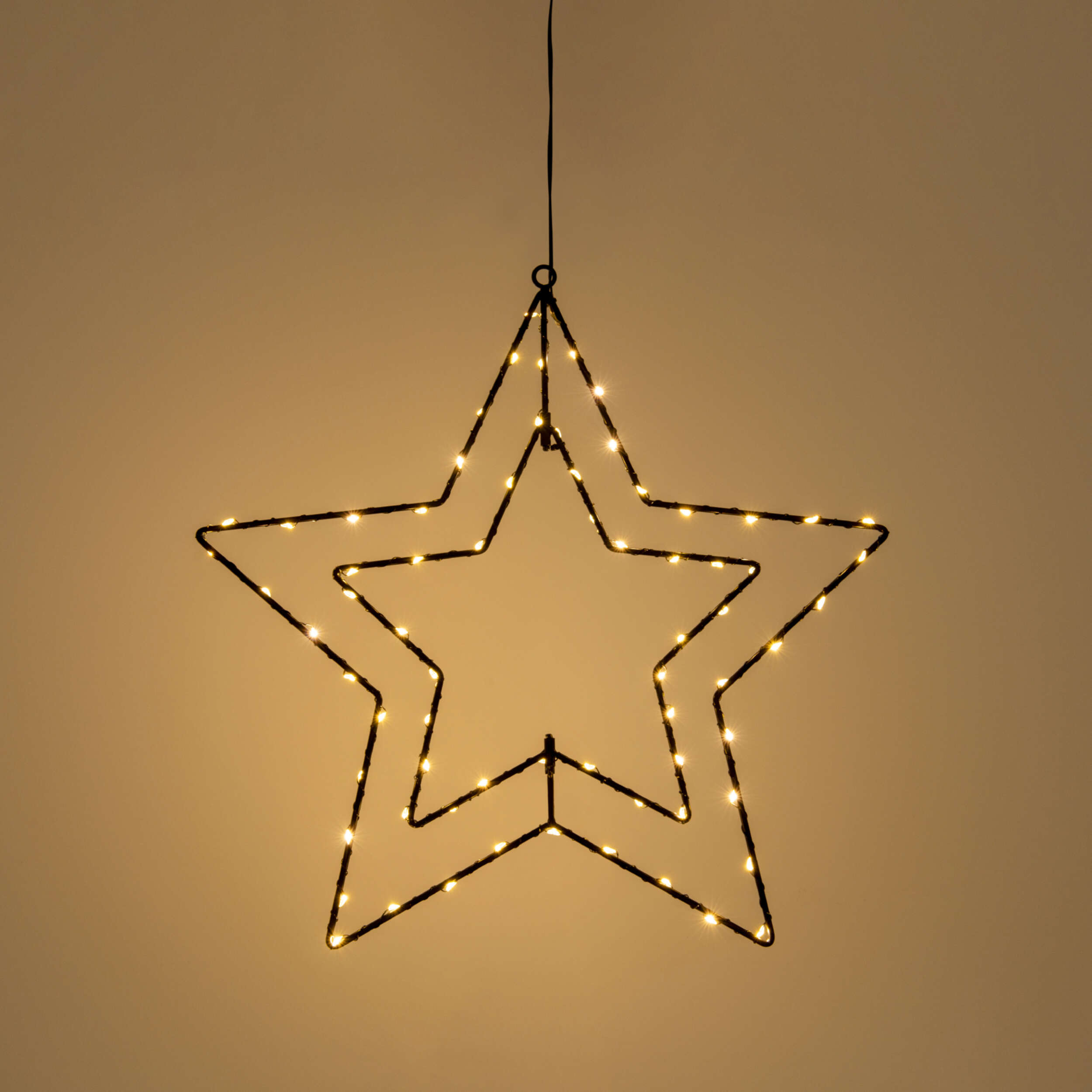 Eine hängende Sternen-Dekoration mit eingebauten Lichtern, die vor einem warmen Hintergrund leuchten.