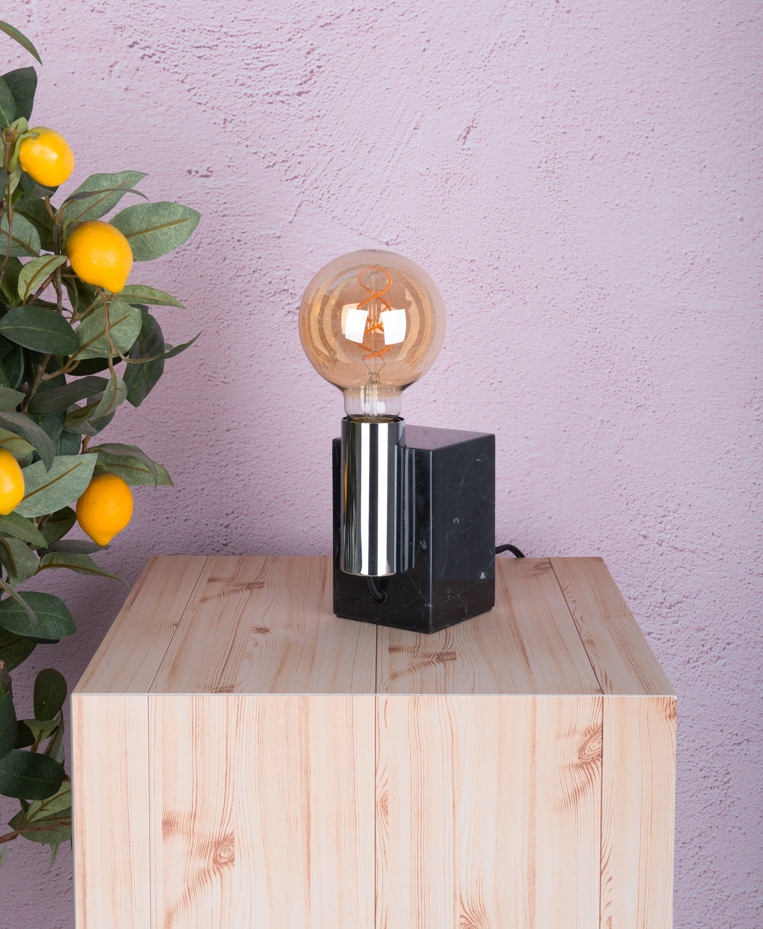 Lampe mit Marmorsockel und Glühbirne. Holztisch, Zitronen, rosa Wand.