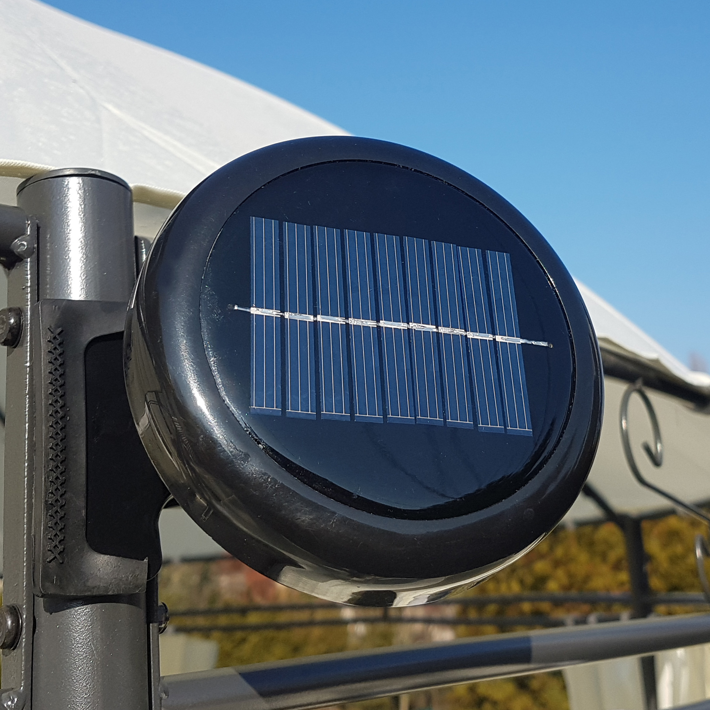Schwarzes Solarpanel an einer Metallstange, montiert an einem Geländer, mit blauem Himmel.
