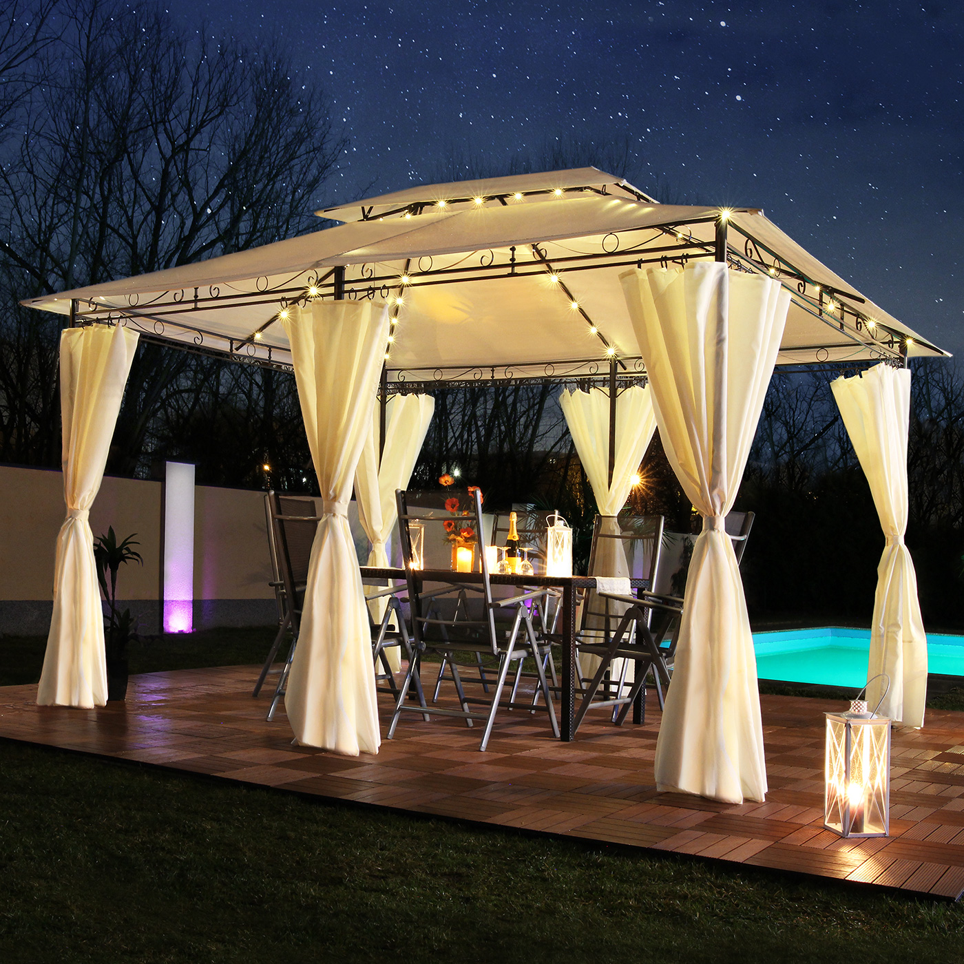 Pavillon mit Lichtern, Tisch, Stühlen und Vorhängen bei Nacht. Pool und Sterne im Hintergrund.