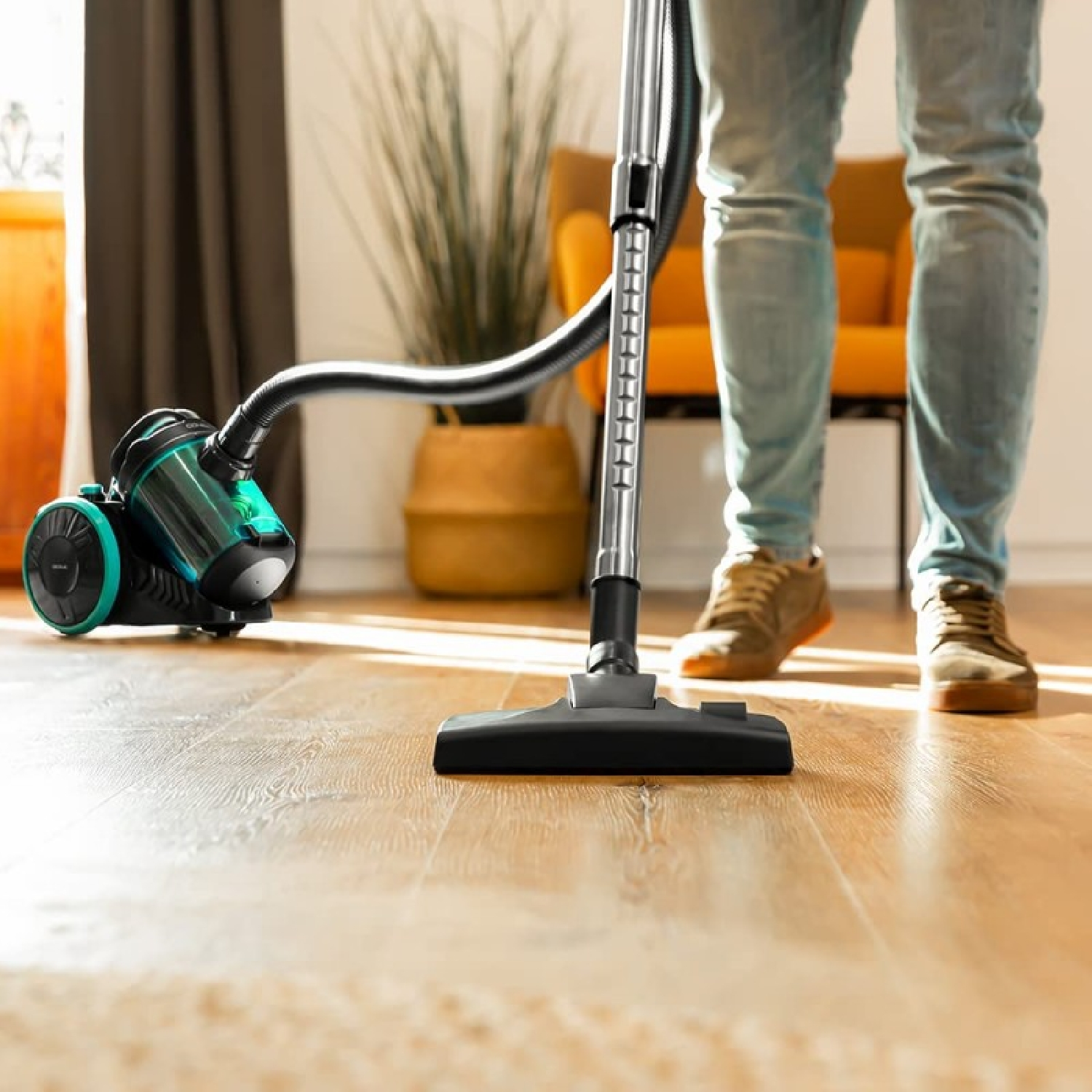 Osoba odkurzająca drewnianą podłogę zielono-czarnym odkurzaczem.