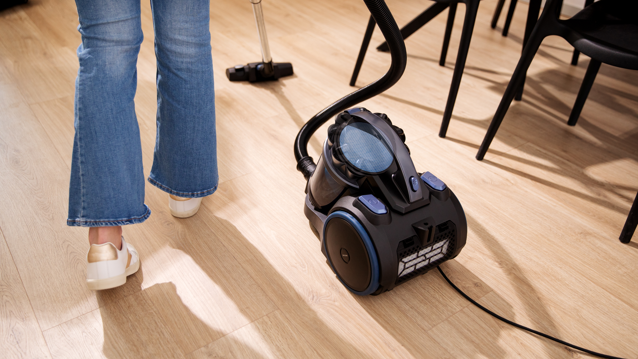 Osoba odkurzająca drewnianą podłogę. Widoczny odkurzacz i stopy.