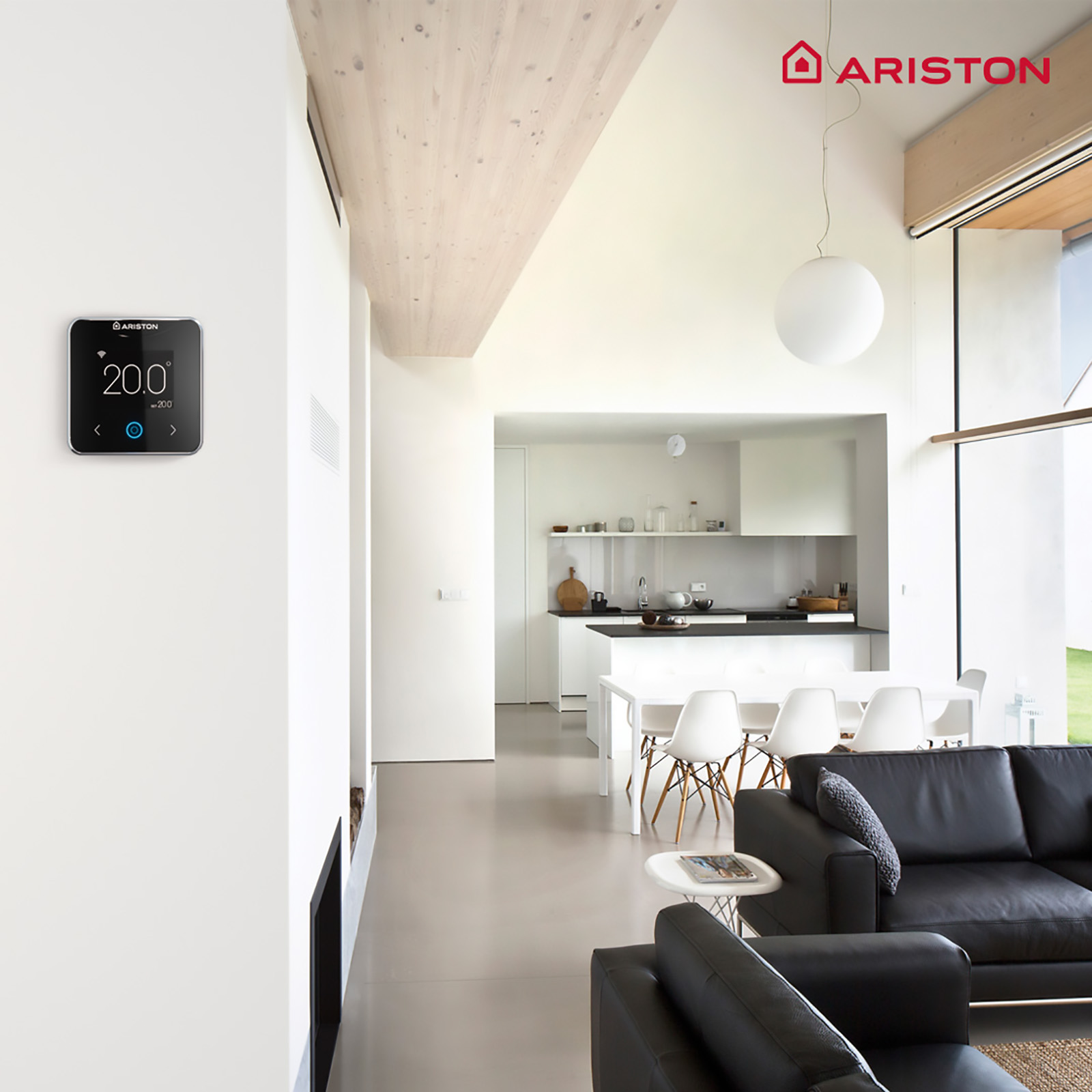 Modernes Wohnzimmer mit einem intelligenten Thermostat an der Wand. Ein schwarzes Sofa und ein großes Fenster.