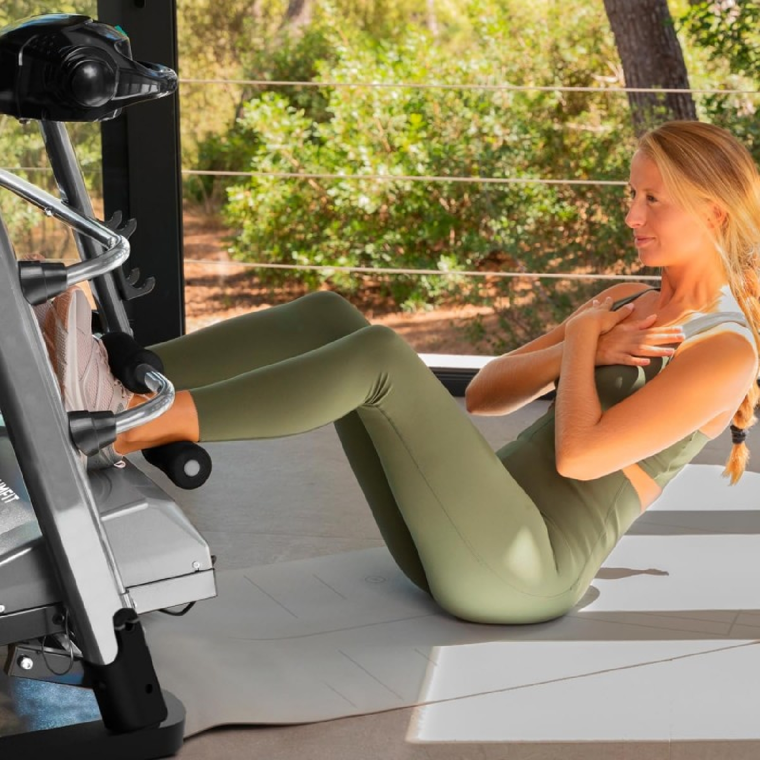 Kobieta robi brzuszki na macie z maszyną do ćwiczeń w tle, w domu.