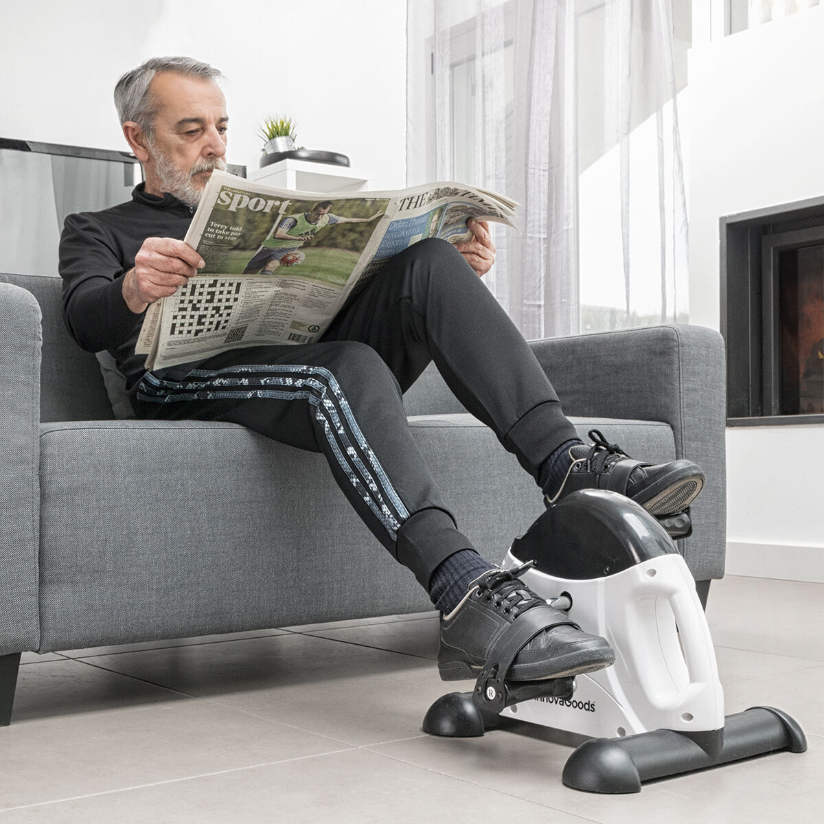 Ein Mann liest Zeitung, während er mit einem Mini-Heimtrainer trainiert.