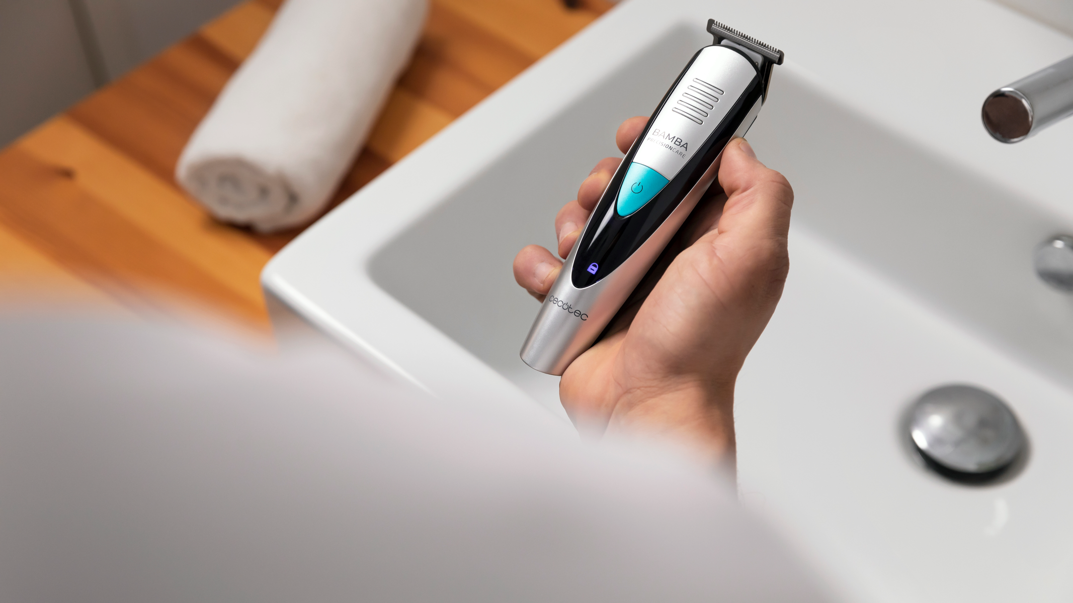 Dłoń mężczyzny trzymająca srebrno-czarną maszynkę do strzyżenia nad białym zlewem.