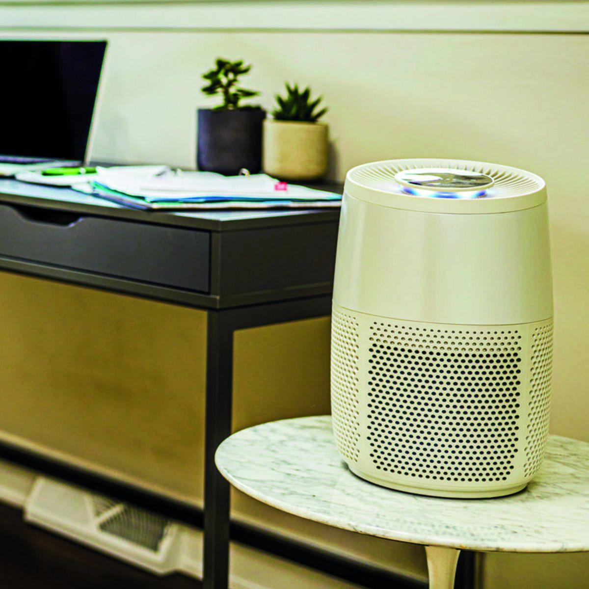 Un purificateur d'air sur une table en marbre. Un bureau avec un ordinateur portable et des plantes en arrière-plan.