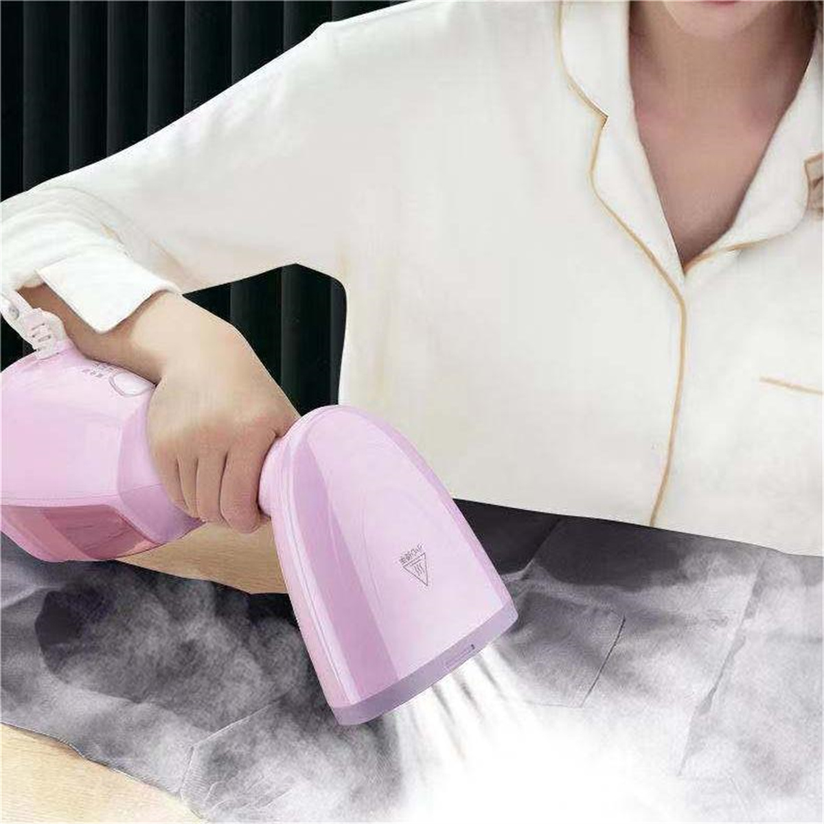Eine Person benutzt einen rosa Kleidungsdampfer. Dampf kommt aus dem Kopf des Dampfers.
