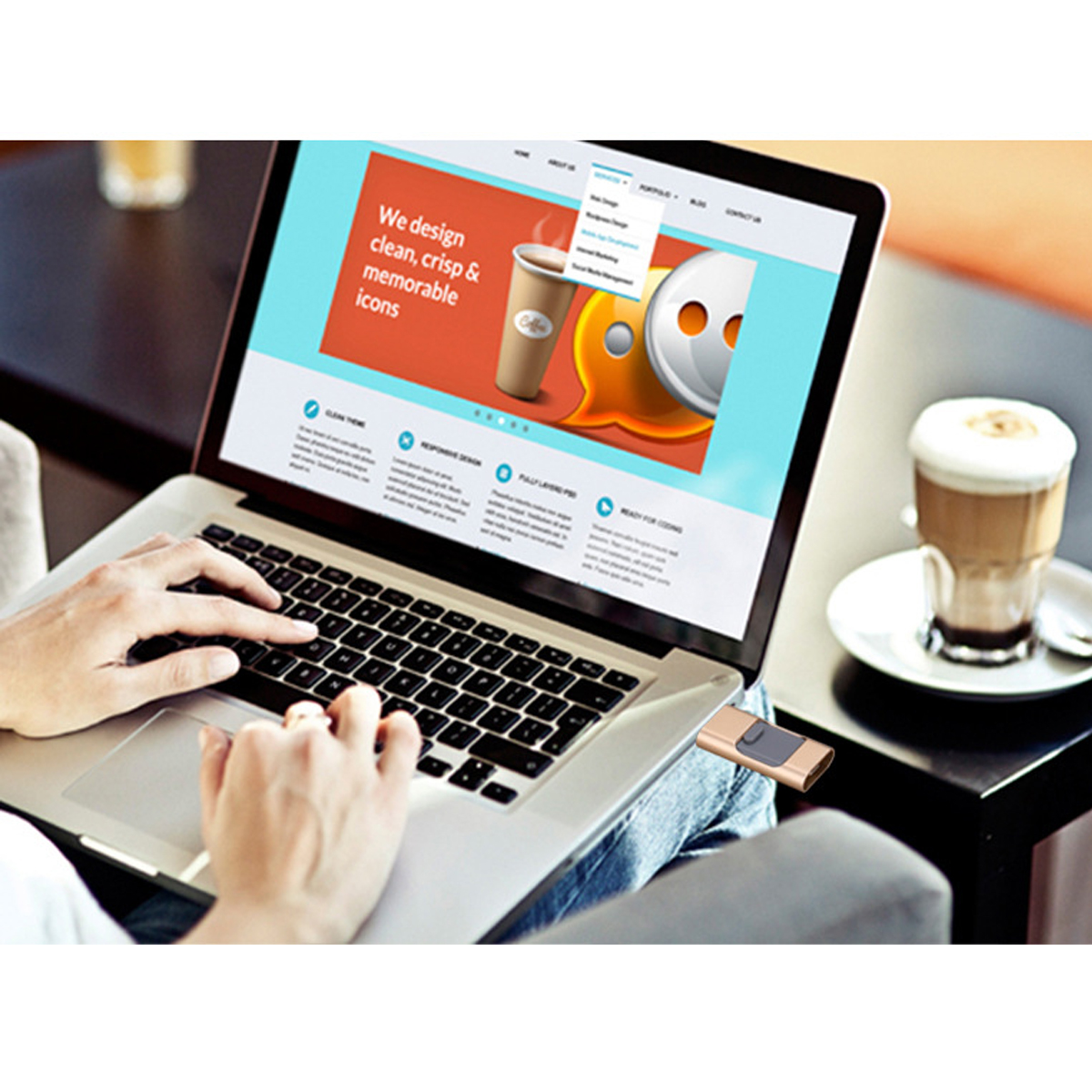 Laptop auf dem Schreibtisch geöffnet, Website-Design auf dem Bildschirm. Person tippt, USB-Stick, Kaffeetasse.