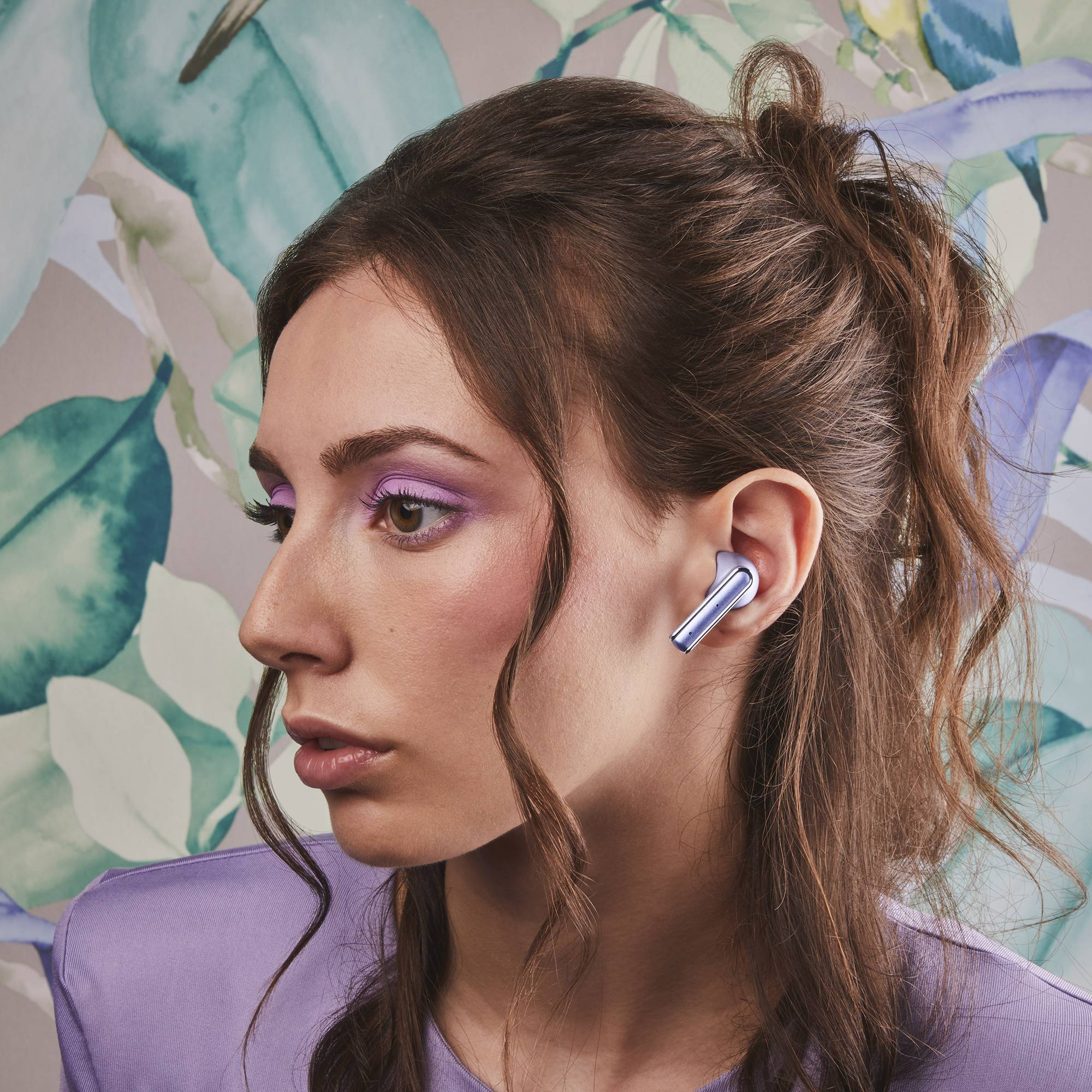 Mujer con auriculares morados, maquillaje de ojos morado y fondo floral.