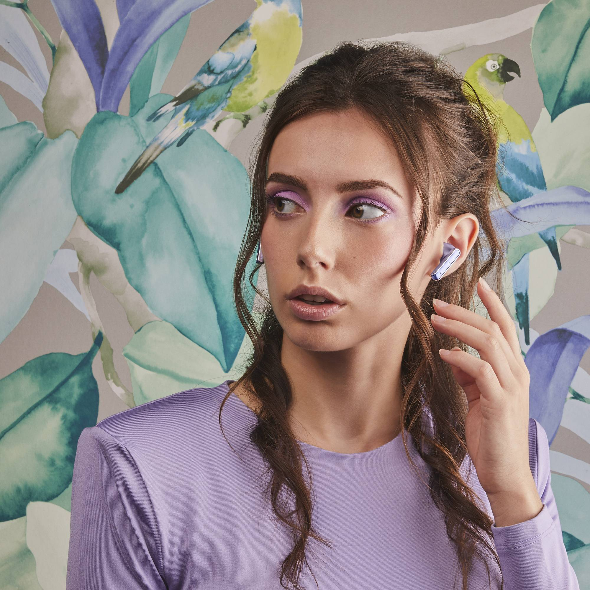 Una mujer con sombra de ojos púrpura lleva auriculares. El fondo tiene un mural floral.