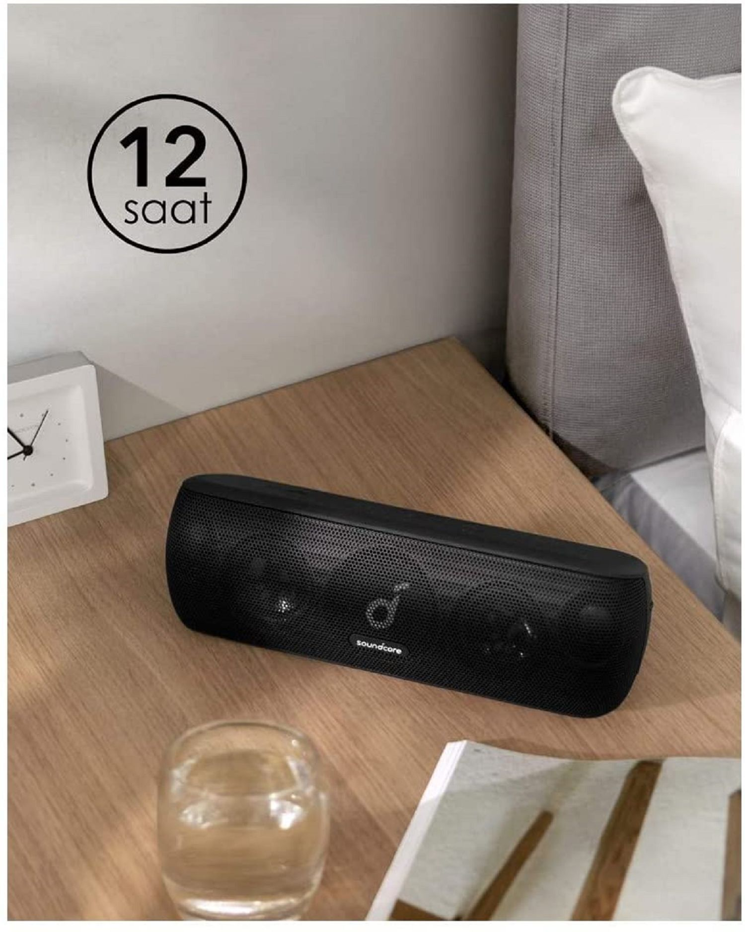 Ahşap bir masada siyah soundcore hoparlör, bir saatin yanında.