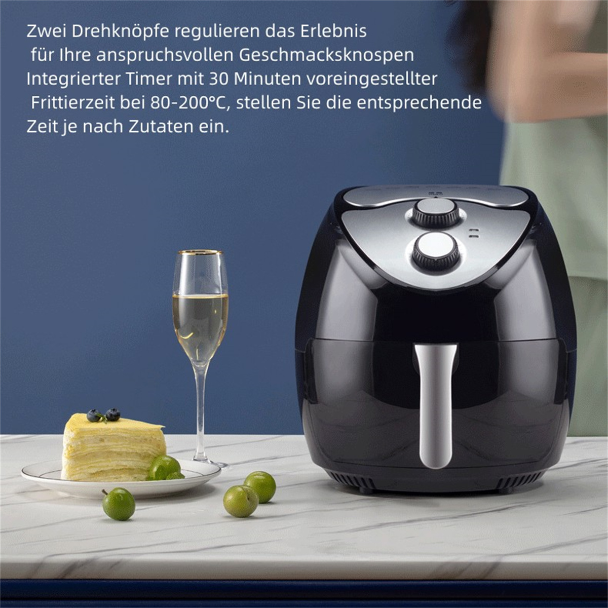Schwarze Heißluftfritteuse mit Weinglas, Kuchen und Obst auf Marmoroberfläche. Text auf Deutsch.