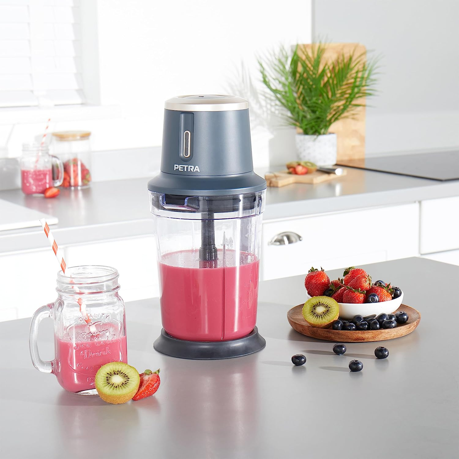 Mixer mit pinkfarbenem Smoothie, Erdbeeren, Blaubeeren, Kiwi. Einmachglas mit Strohhalm und Getränk.