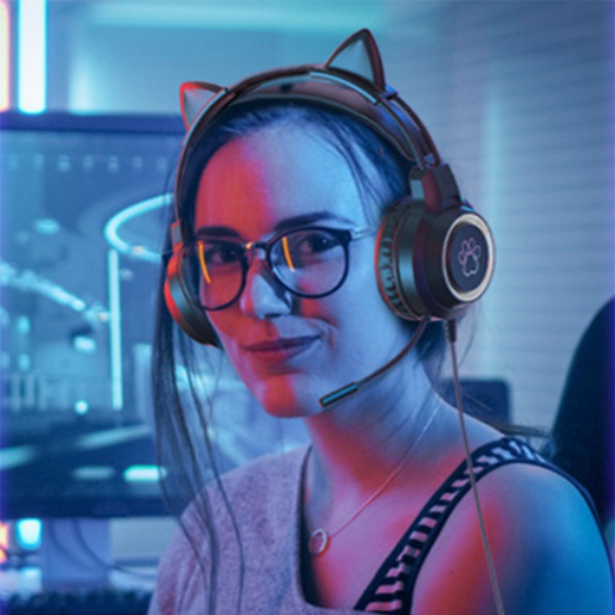 Eine Frau mit Katzenohrkopfhörern lächelt, trägt eine Brille. Ein Computermonitor ist im Hintergrund.
