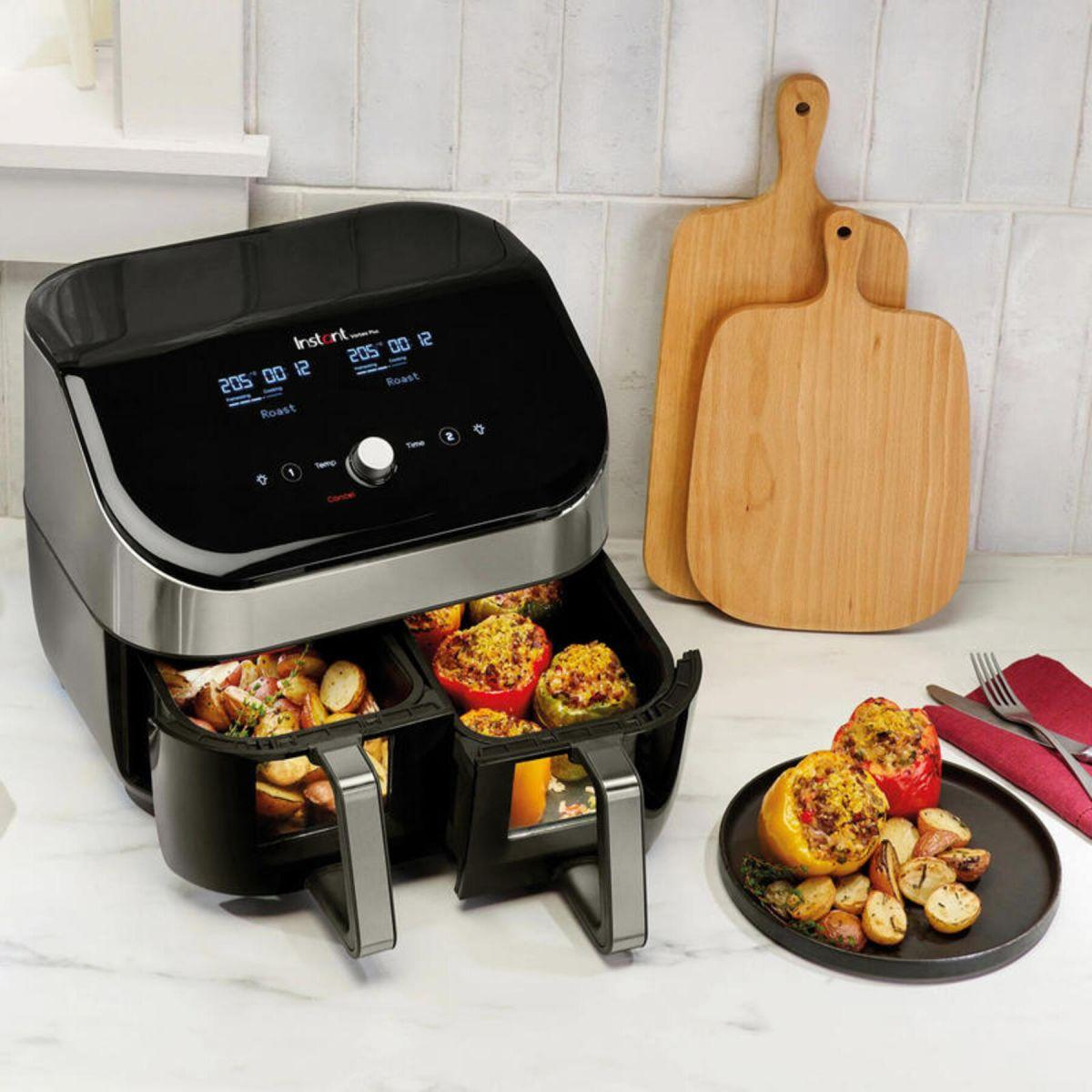 An air fryer with food inside and two cutting boards on a countertop with a kitchen in the background.